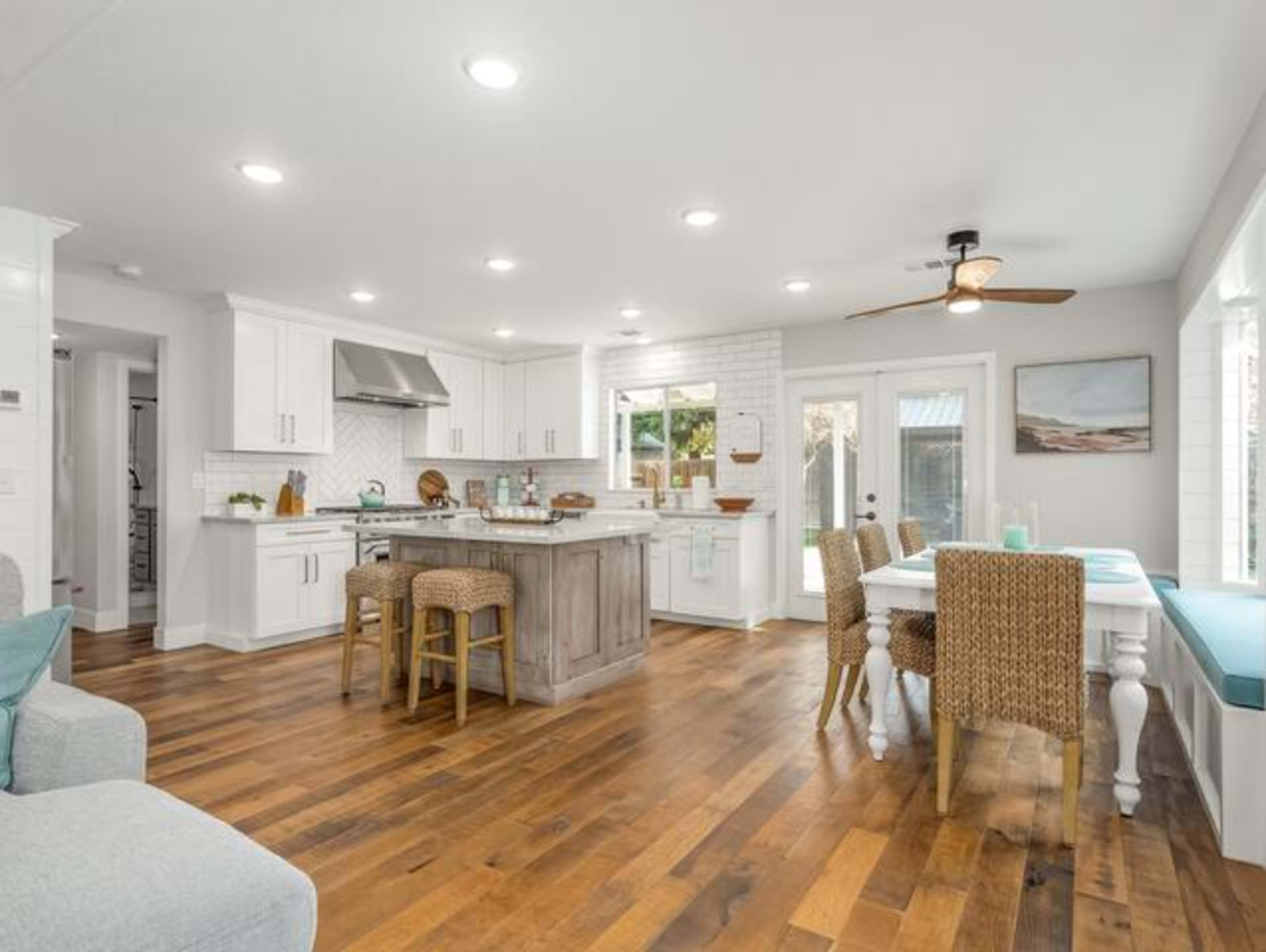 A modern kitchen and dining area features white cabinetry, a large island with bar stools, and a wooden dining table beside a window.