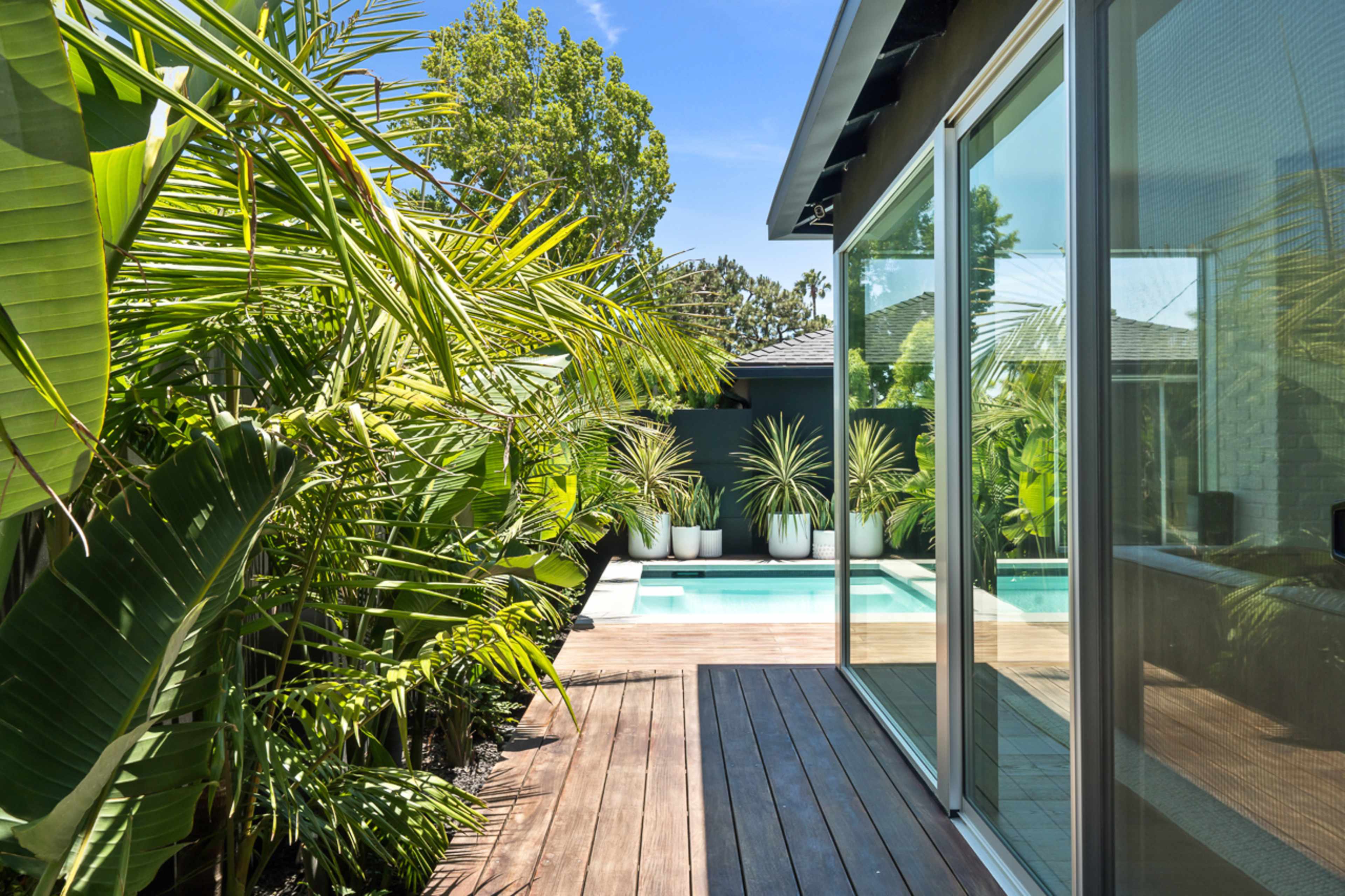 A pathway lined with greenery leads to a pool area visible through large glass doors.