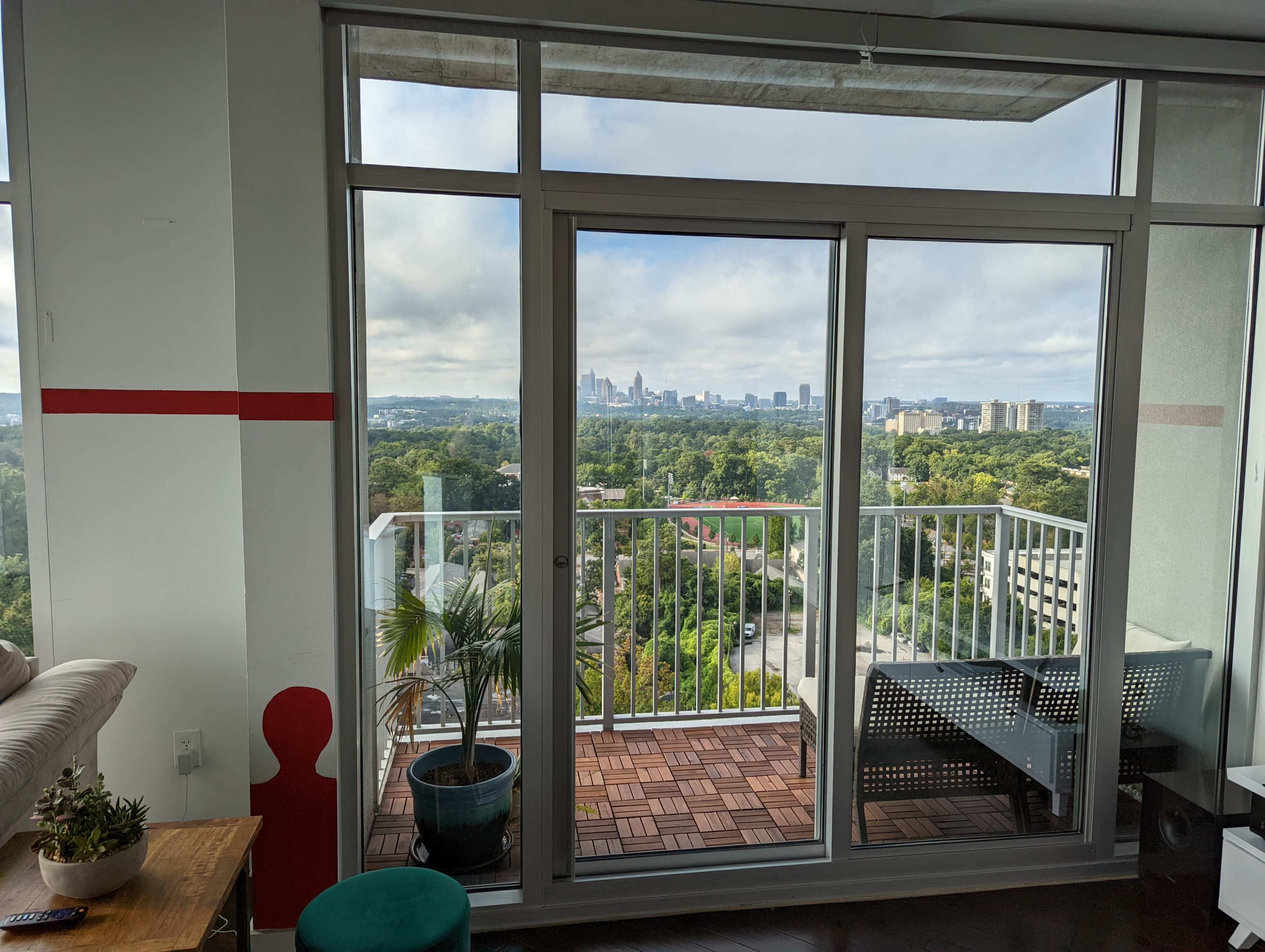 A modern living space with large glass doors opening to a balcony that overlooks a city skyline and green landscape.