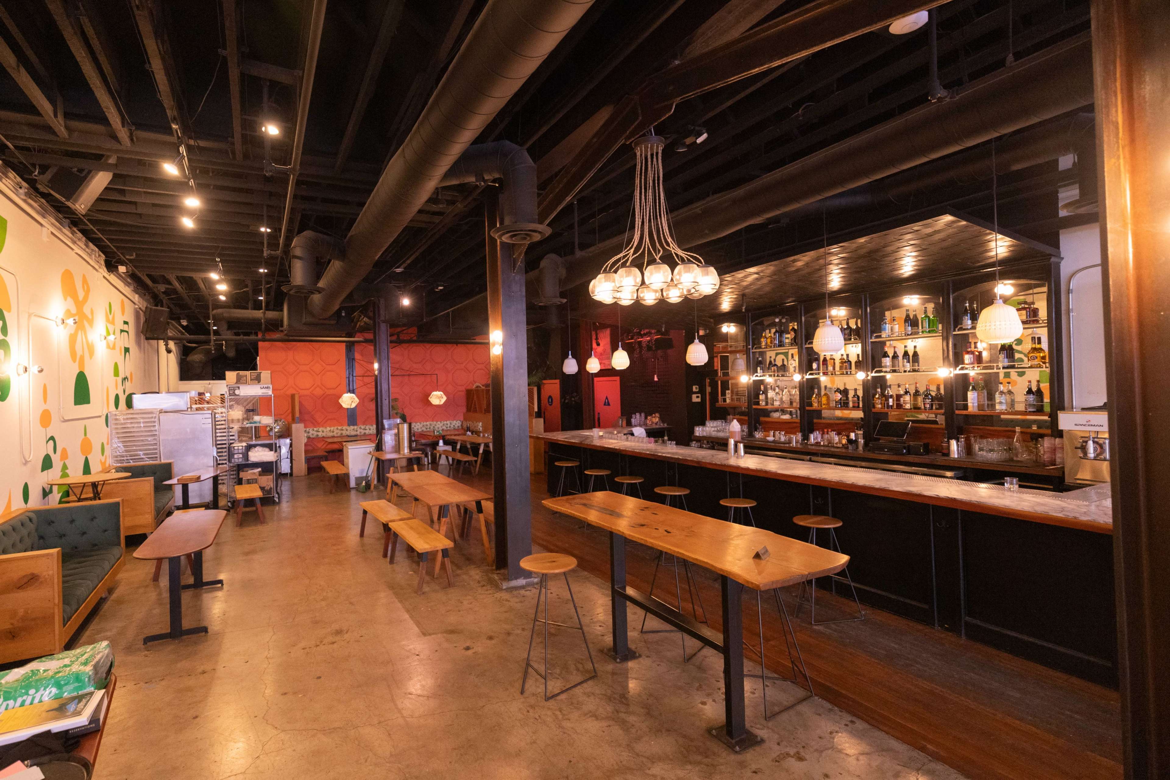 The image shows a spacious restaurant interior with a bar, wooden tables, and various seating arrangements.