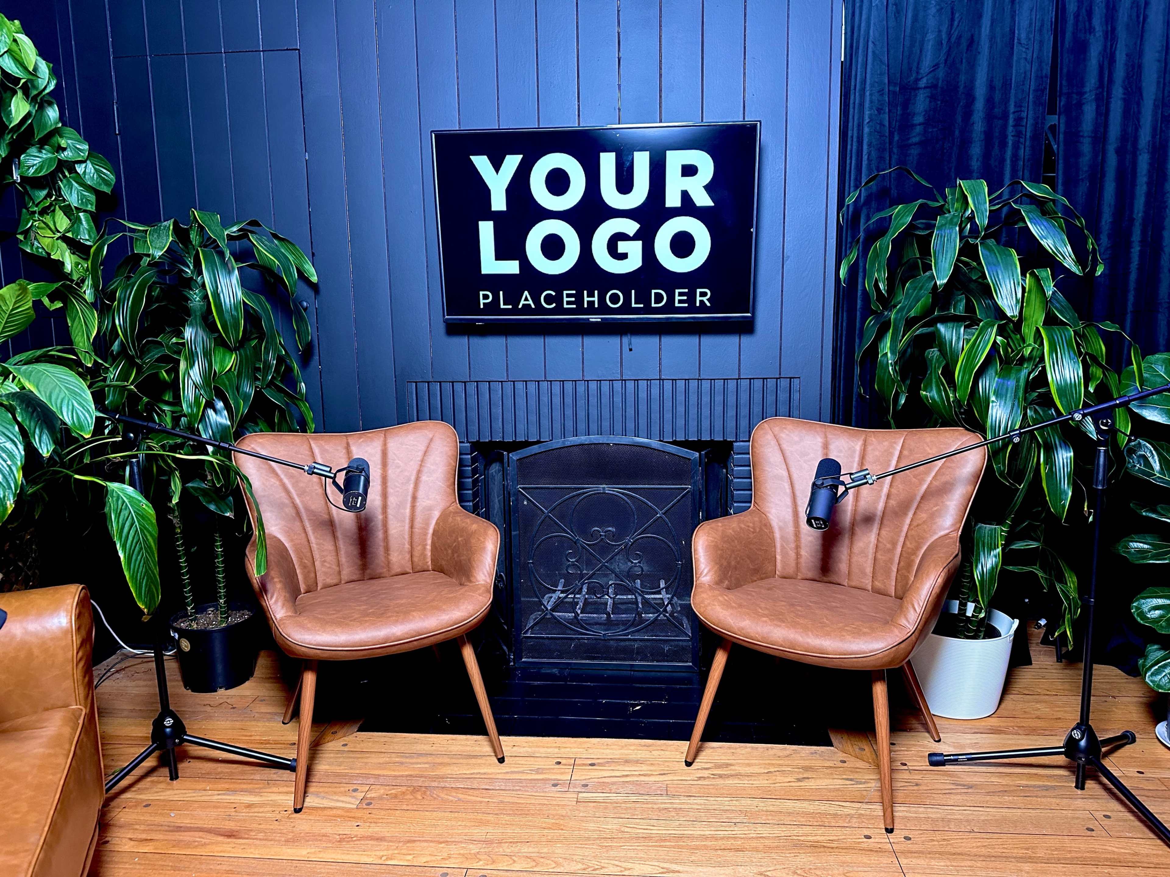 The image shows a cozy indoor setting with two brown leather armchairs equipped with microphones, flanked by potted plants, and a wall-mounted screen displaying the text "YOUR LOGO PLACEHOLDER."