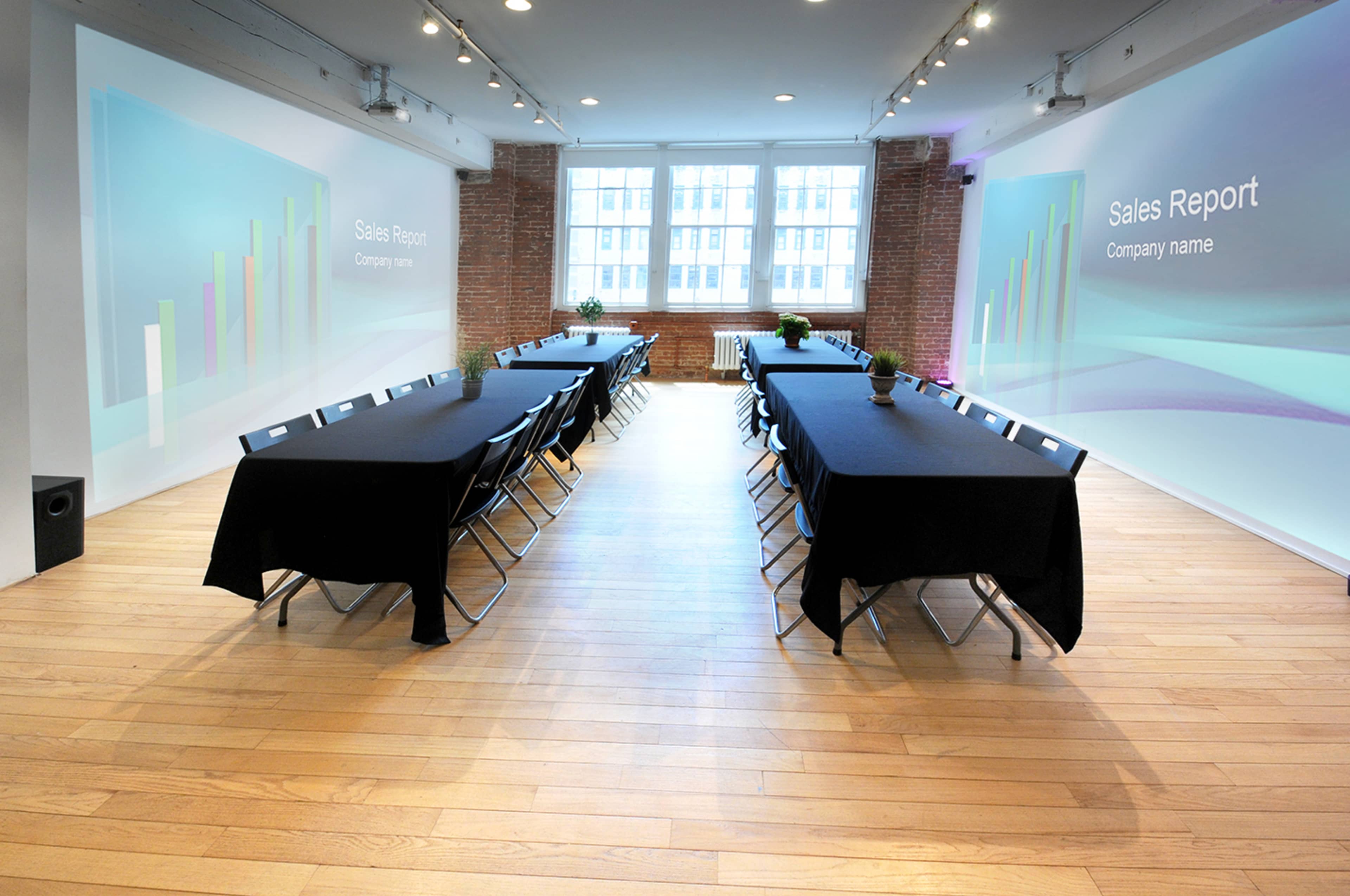 A conference room with two rows of tables set up for a meeting, featuring digital screens displaying "Sales Report" on the walls.