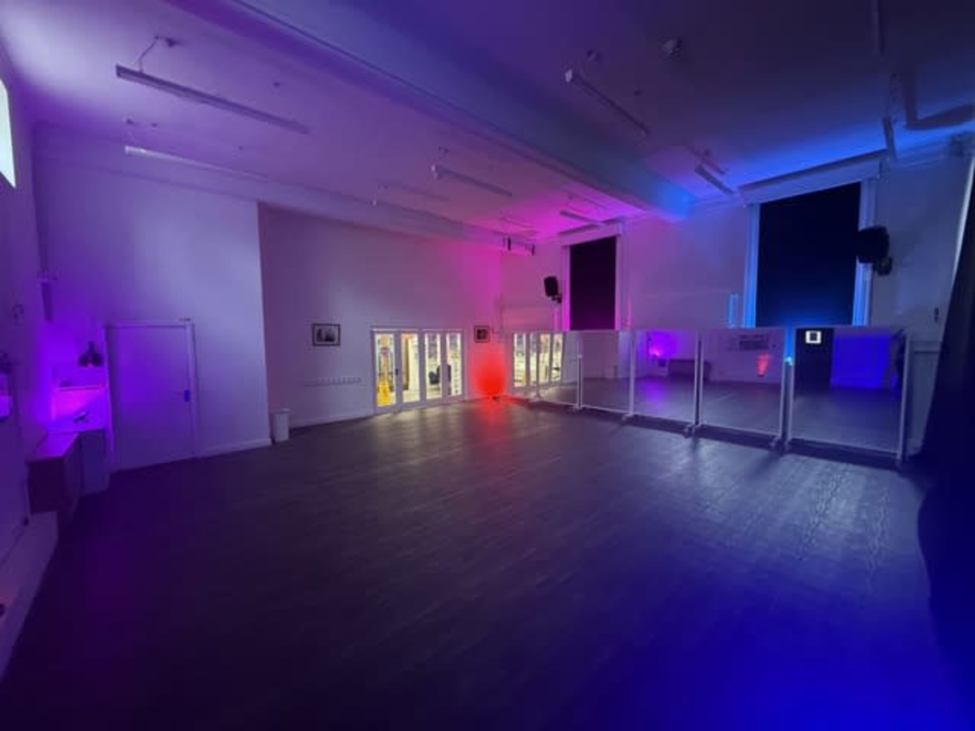 The image shows a large, empty room with colorful lighting and large windows on one side.