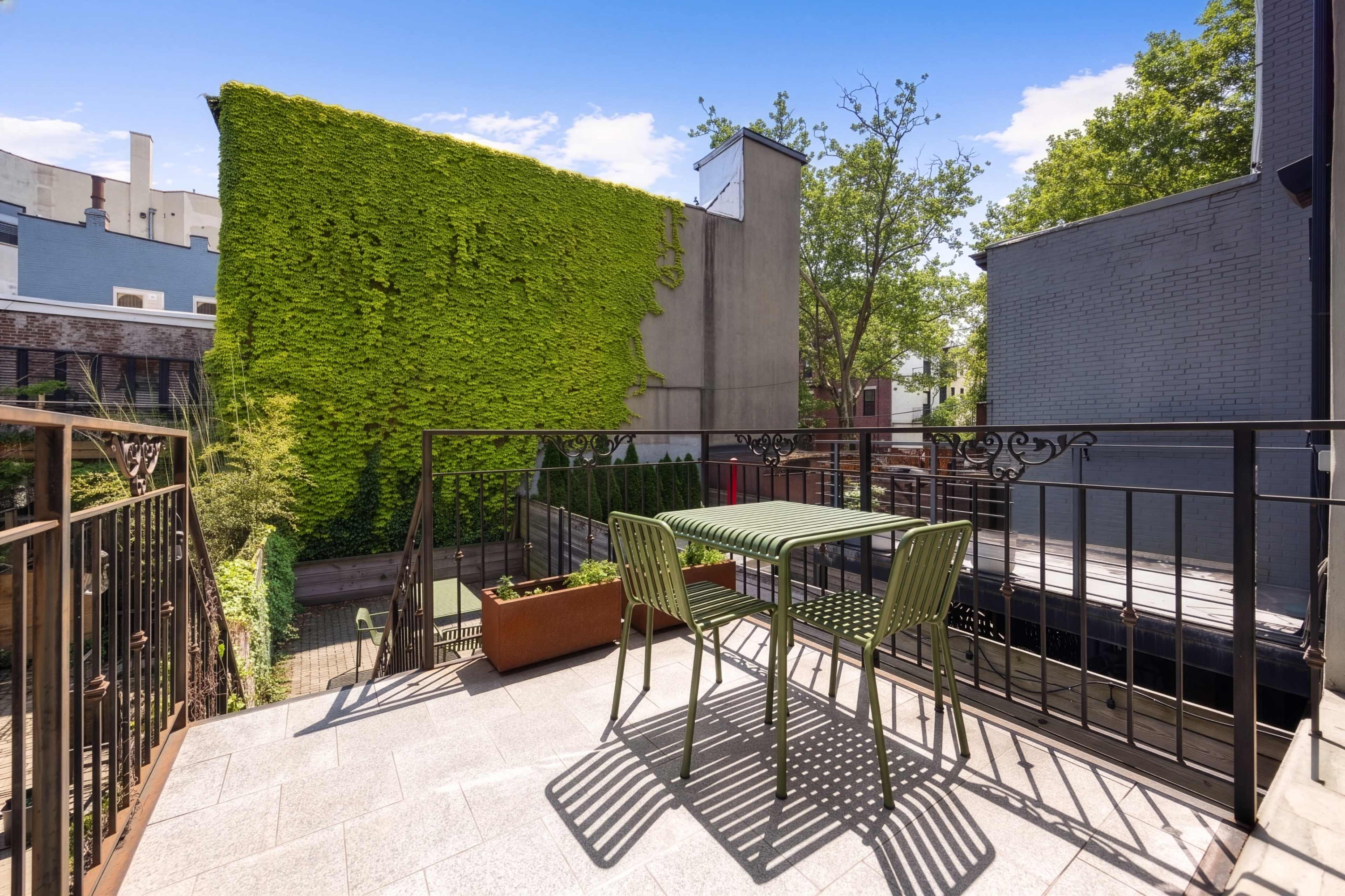 A small outdoor patio features a table and chairs, surrounded by green plants and a wall covered in ivy.
