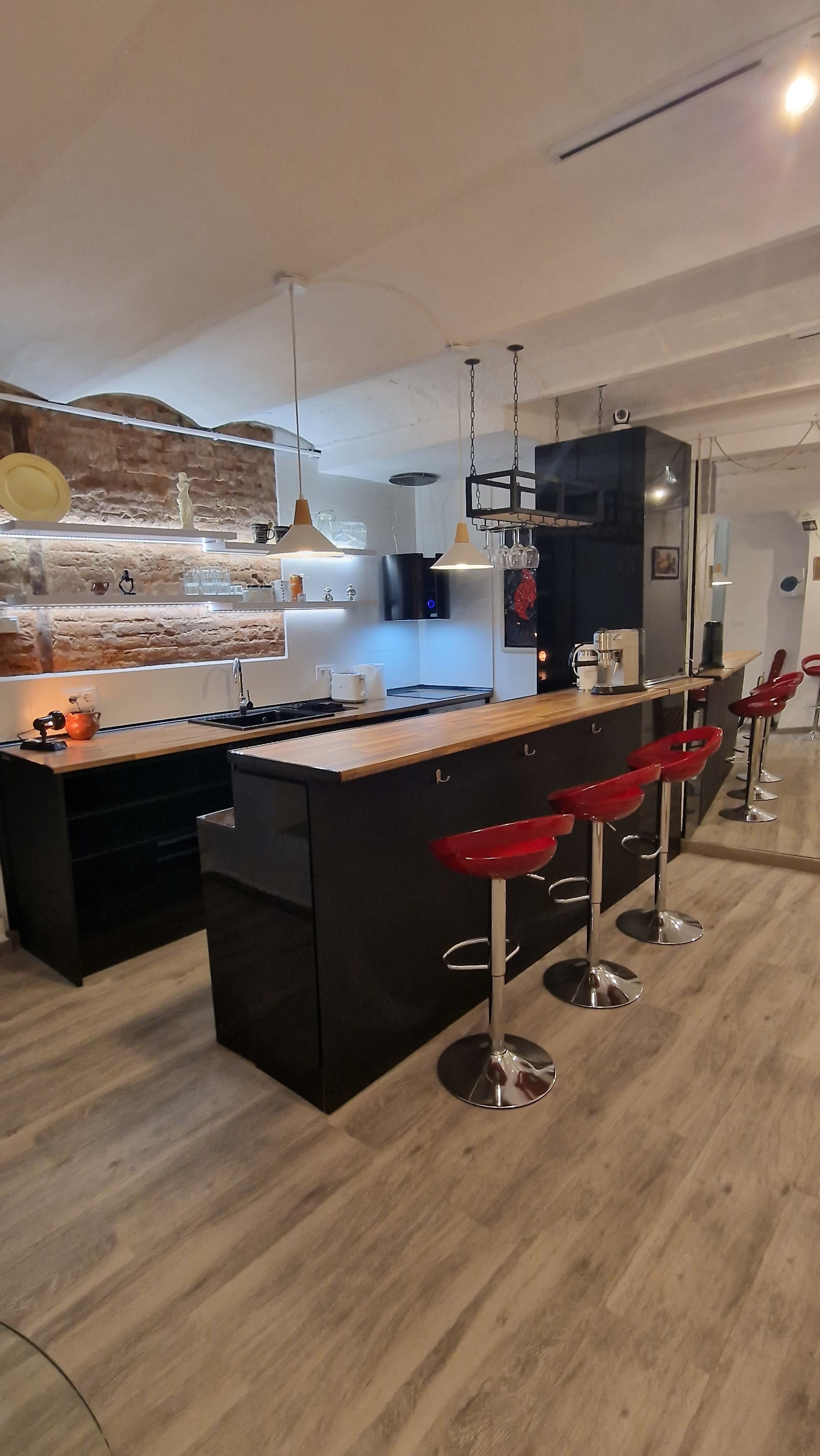 A modern kitchen features a central island with a wooden countertop and four red bar stools, set against a backdrop of stone walls and sleek cabinetry.