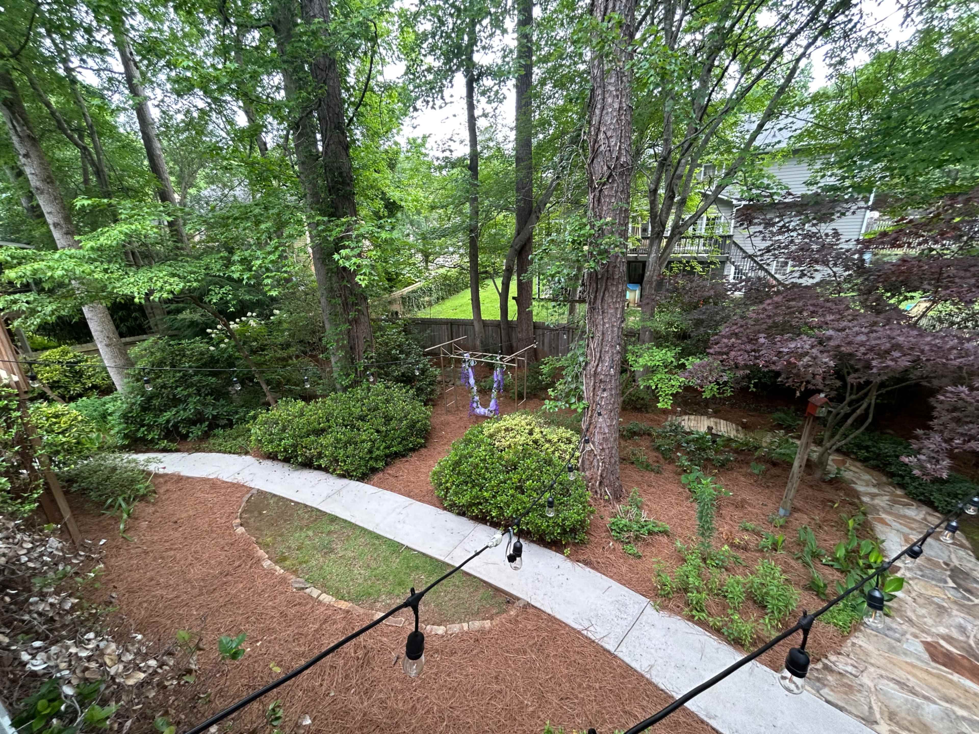A winding concrete path leads through a landscaped garden filled with trees, shrubs, and a small lawn area.