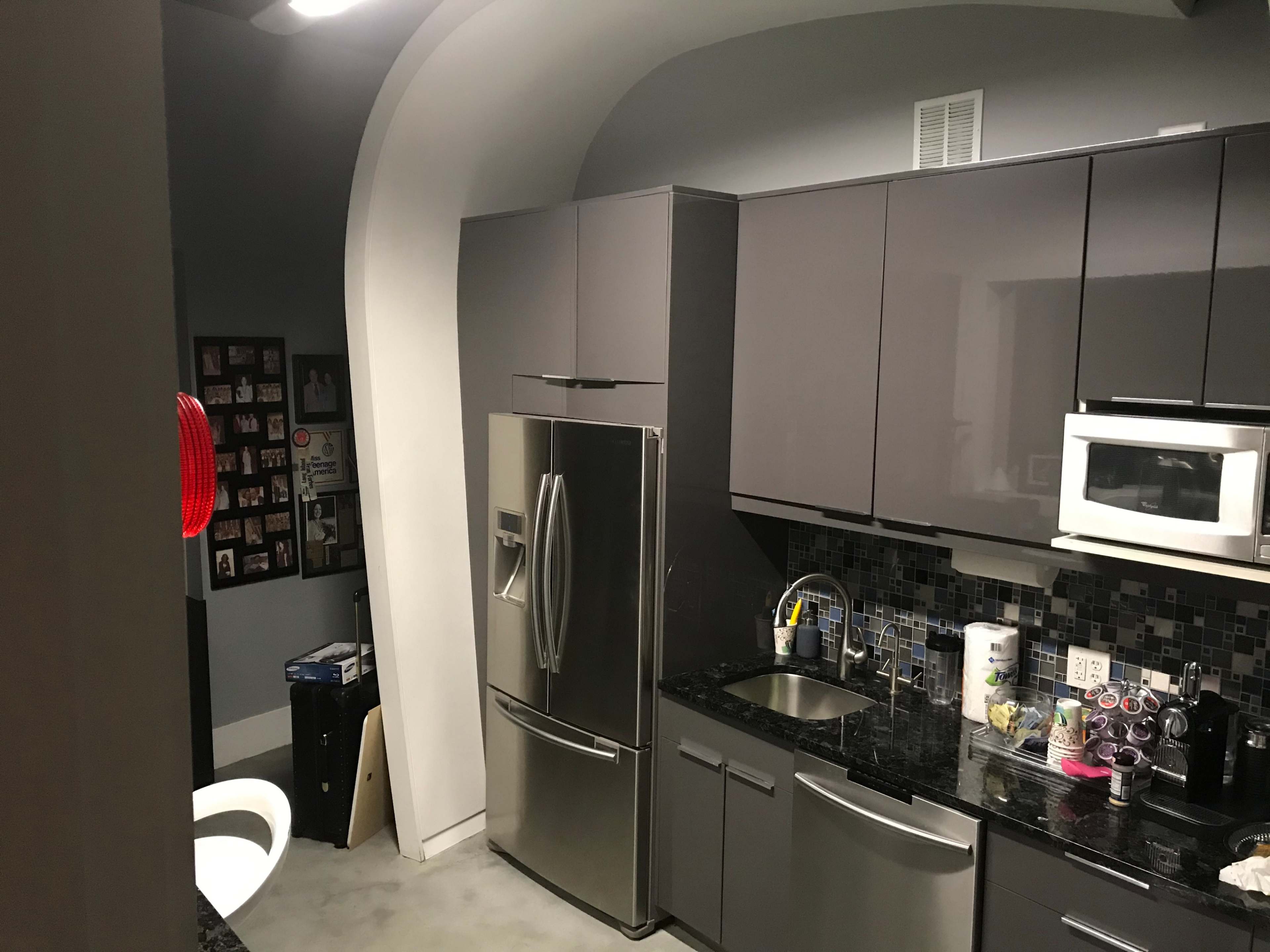 A modern kitchen features stainless steel appliances, dark cabinetry, and a mosaic tile backsplash.