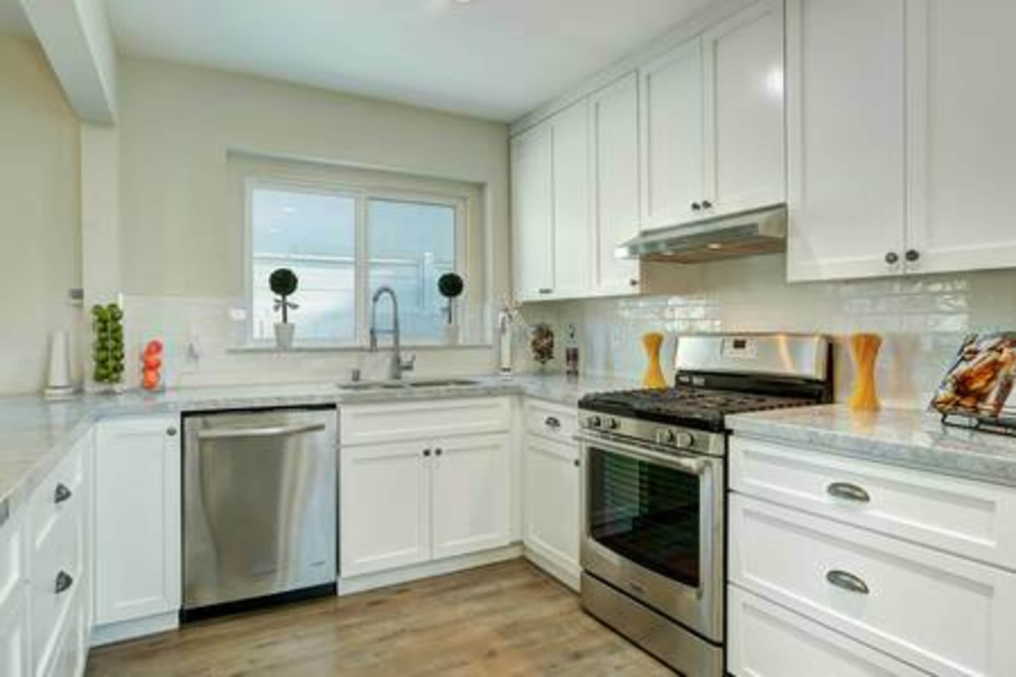 A modern kitchen featuring white cabinetry, stainless steel appliances, and a marble countertop.