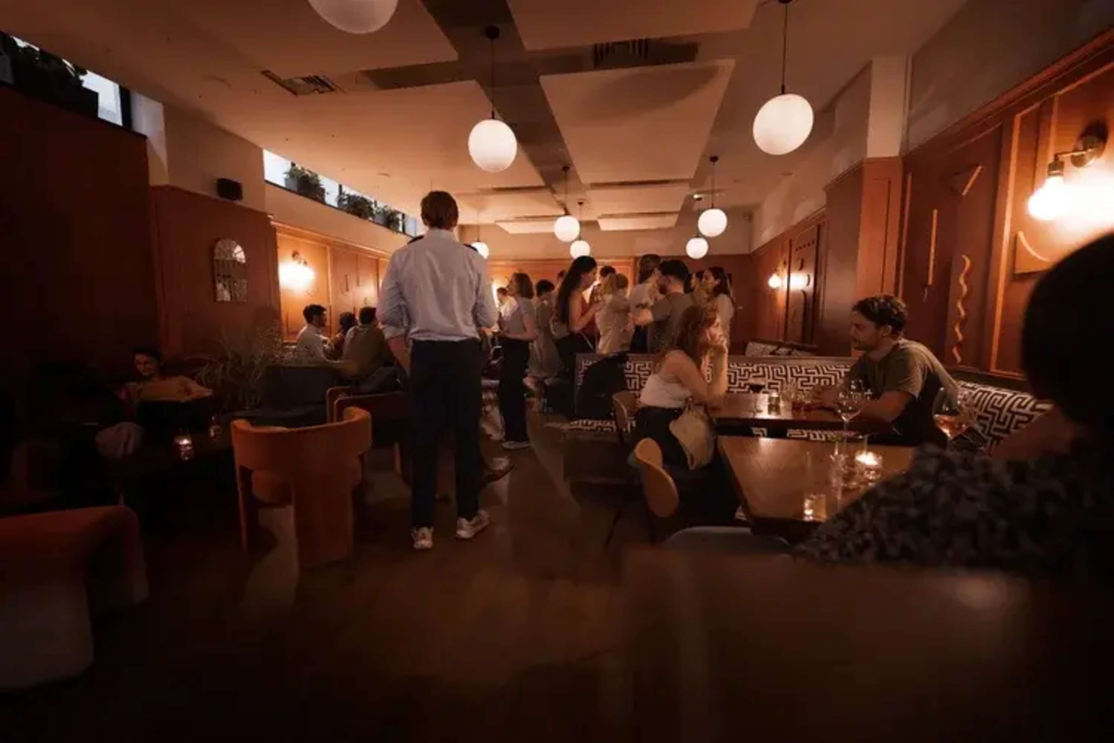 A lively bar scene features patrons mingling and seated at tables under soft lighting from hanging globes.