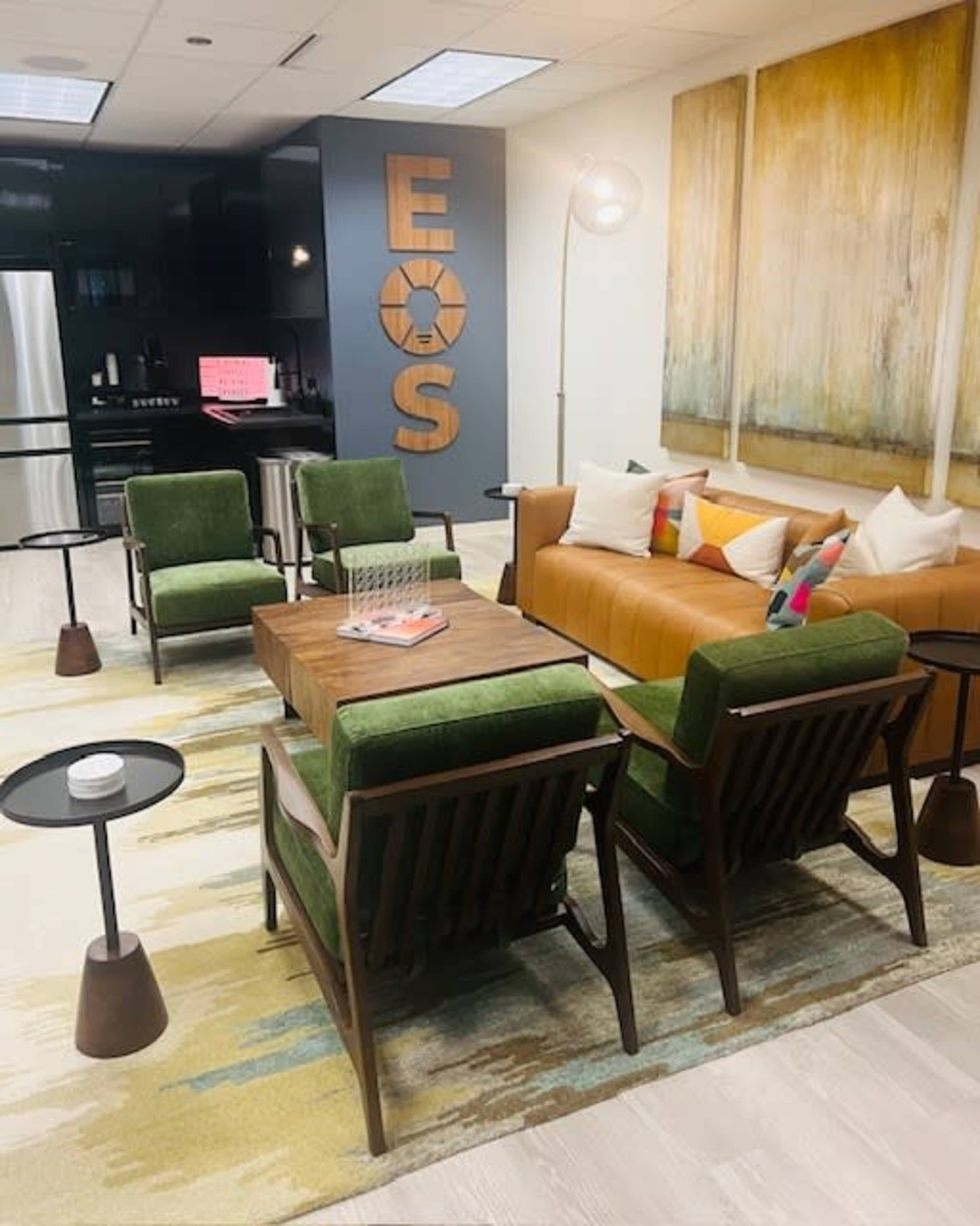 A modern lounge area featuring green upholstered chairs, a wooden coffee table, a brown sofa, and large abstract paintings on the wall.