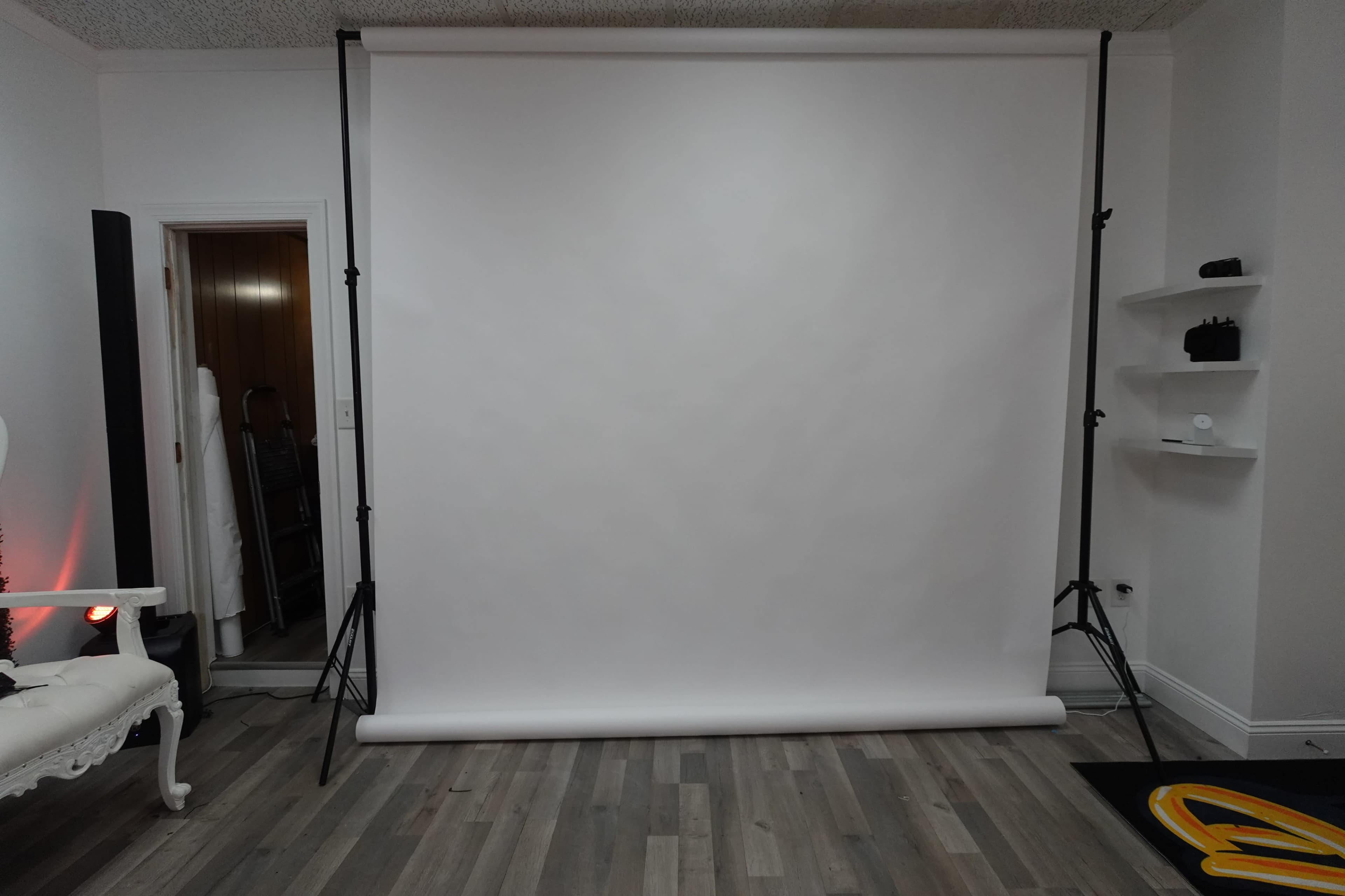 A plain white backdrop is set up in a room with wooden flooring and minimal decor.
