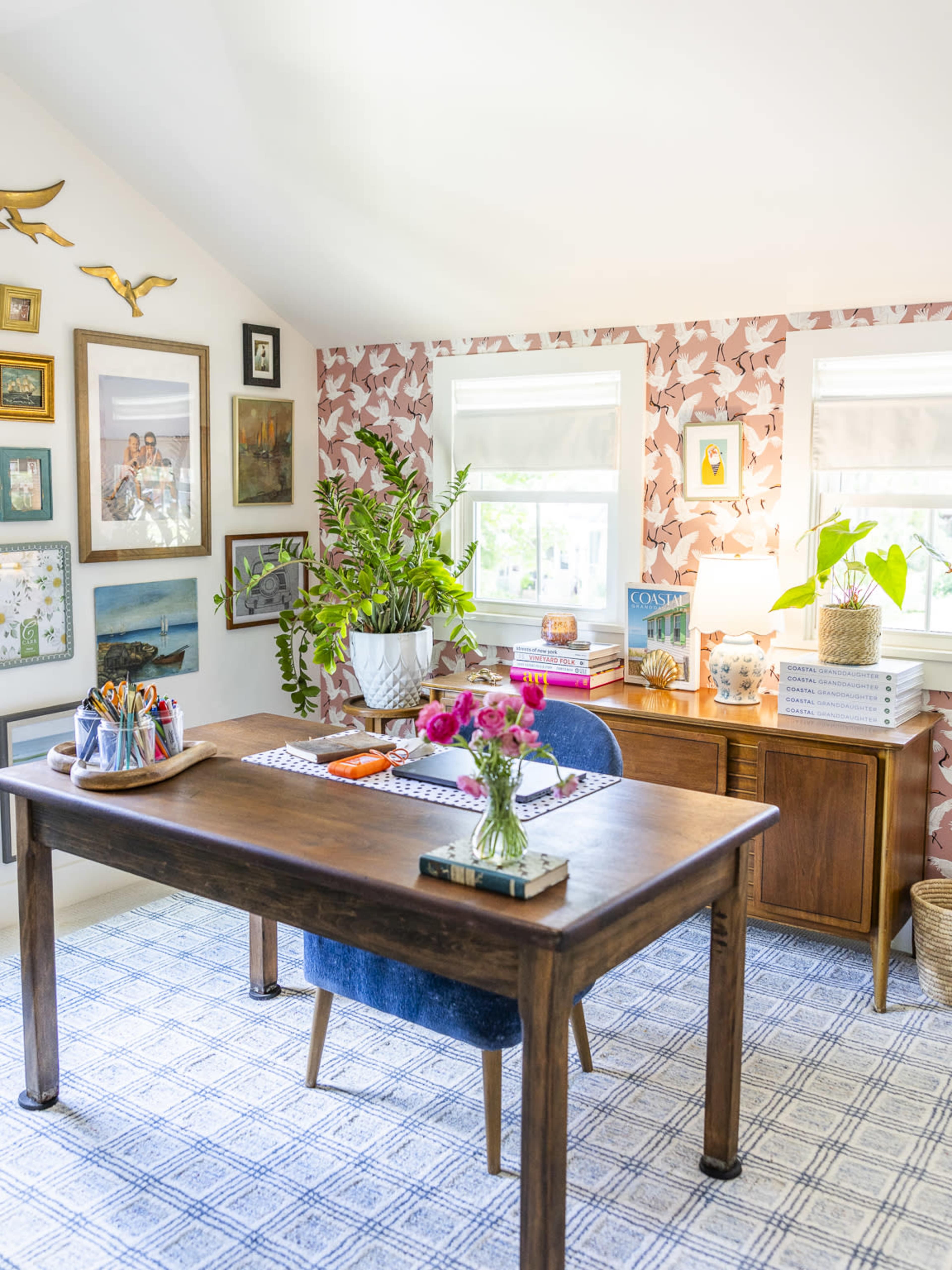 A well-designed home office features a wooden desk, blue chair, potted plants, and colorful artwork on the walls.