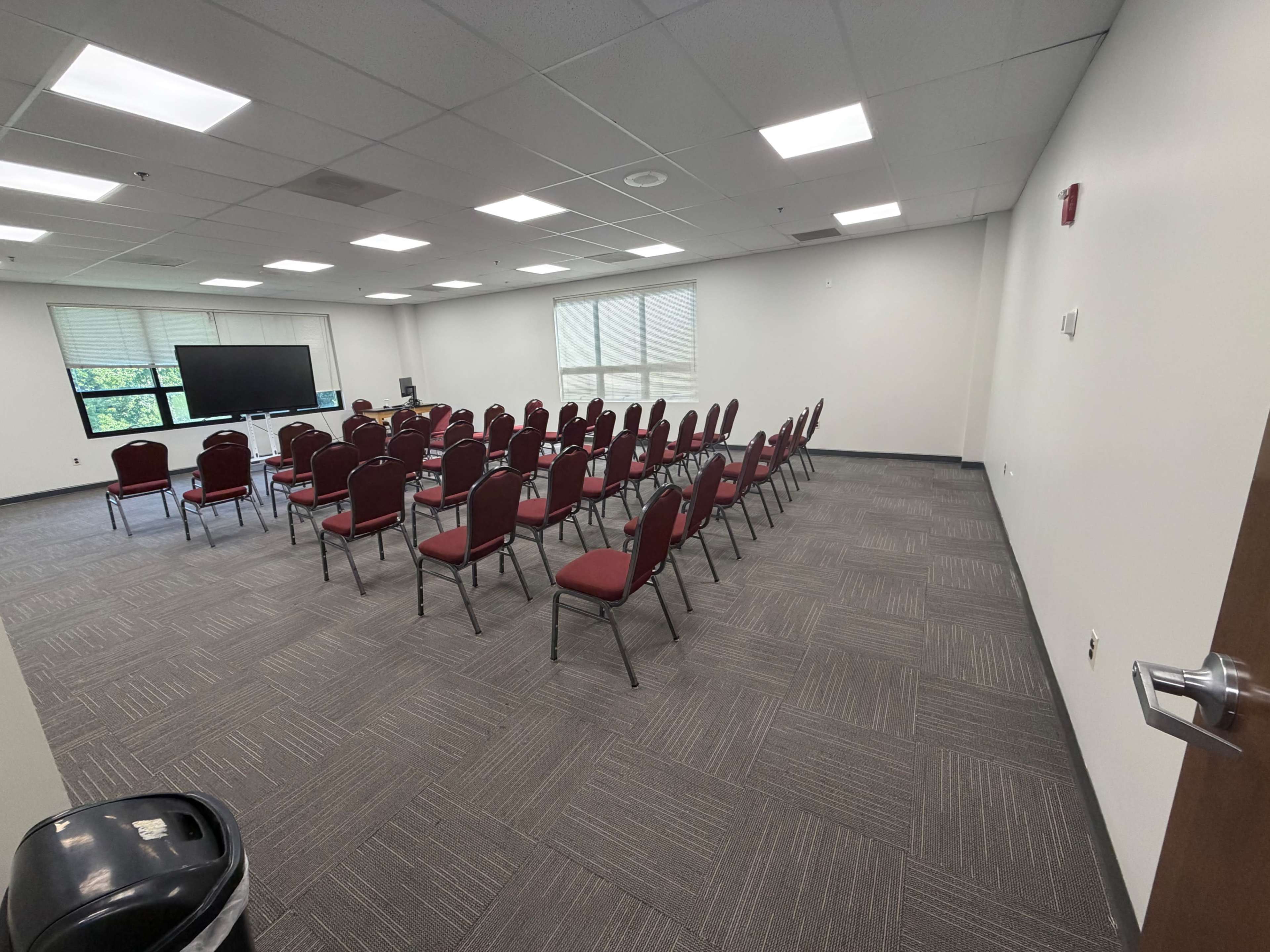 The image shows a conference room set up with rows of red chairs facing a large screen.