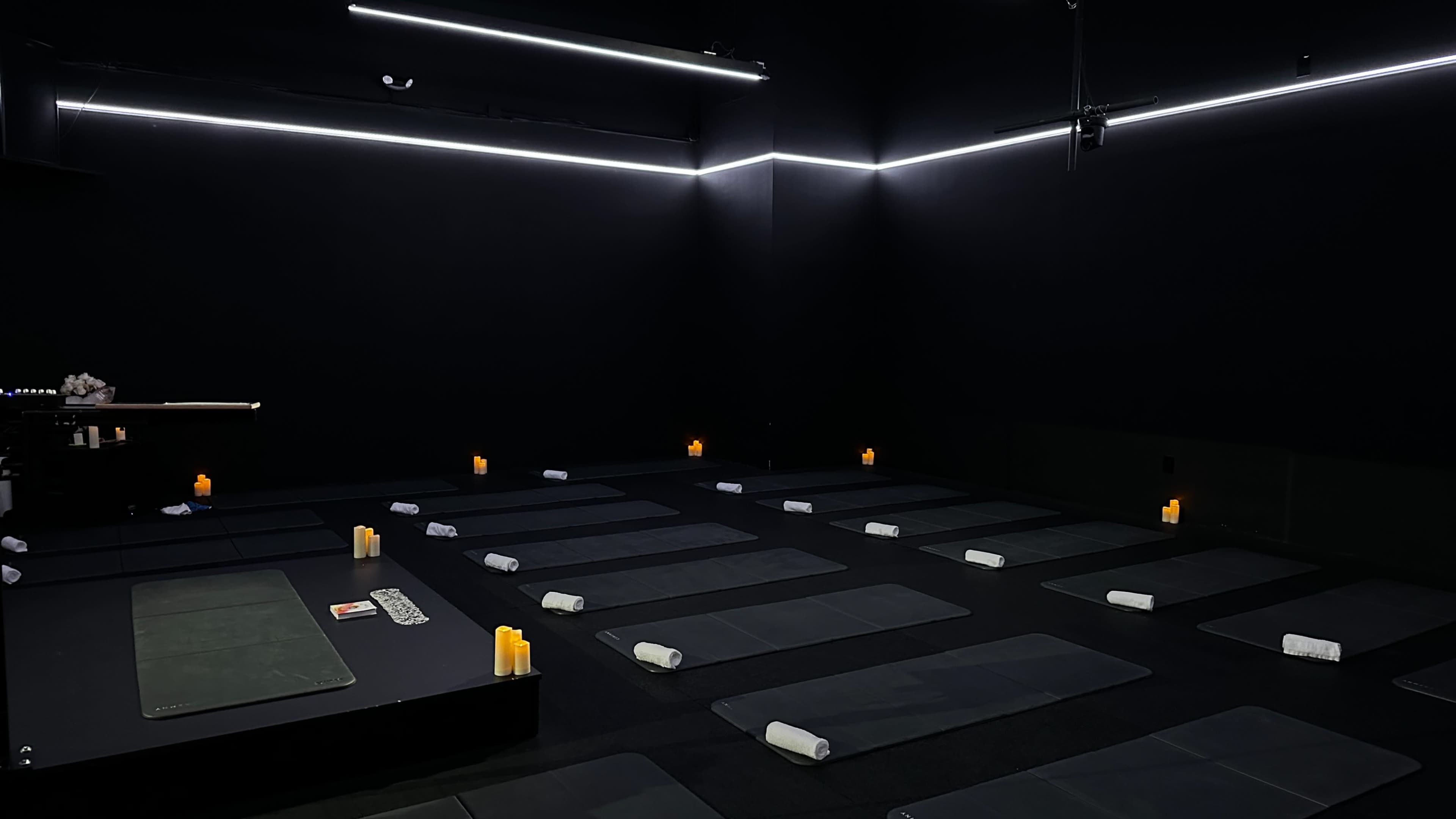 The image shows a dimly lit yoga studio with multiple exercise mats arranged neatly on the floor, and candles placed around the room.