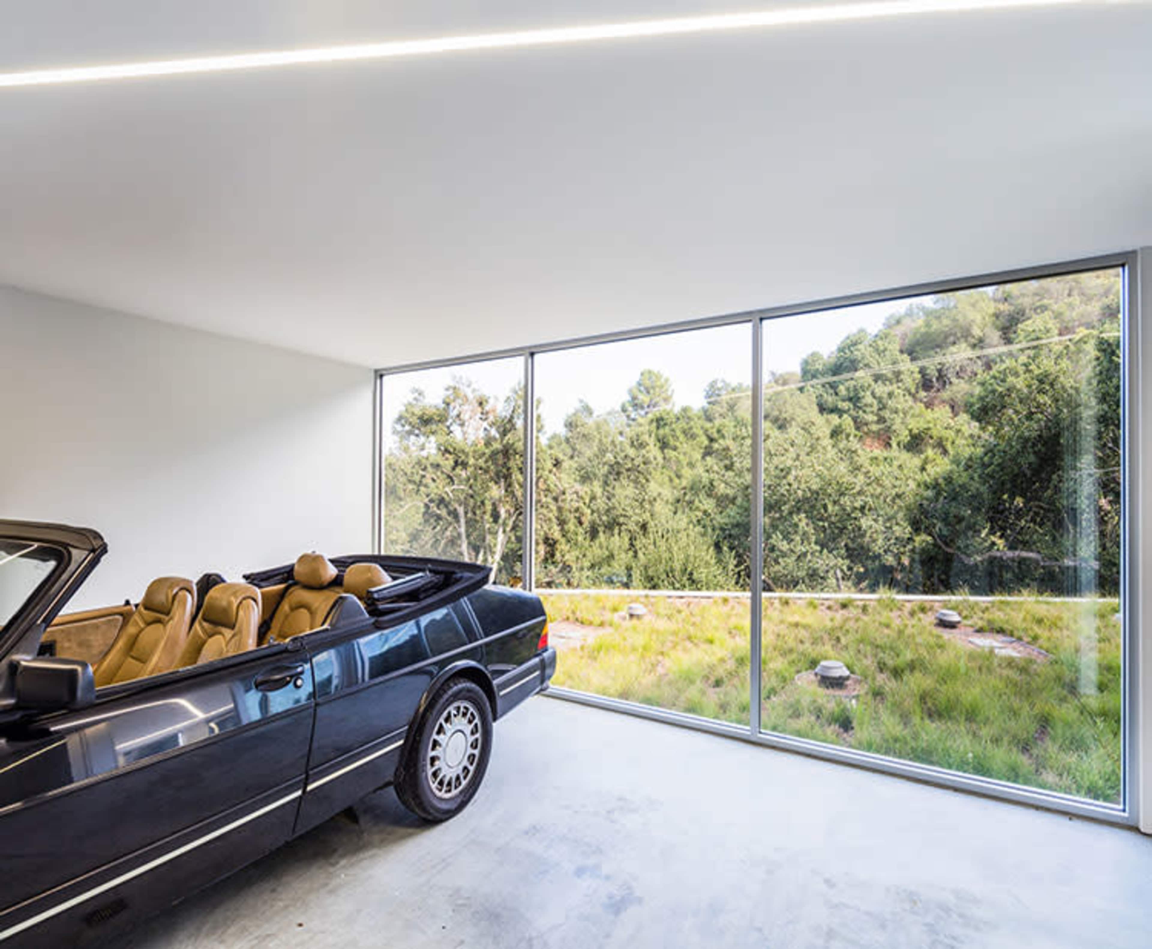 A black convertible car is parked inside a modern room with large windows overlooking a green landscape.