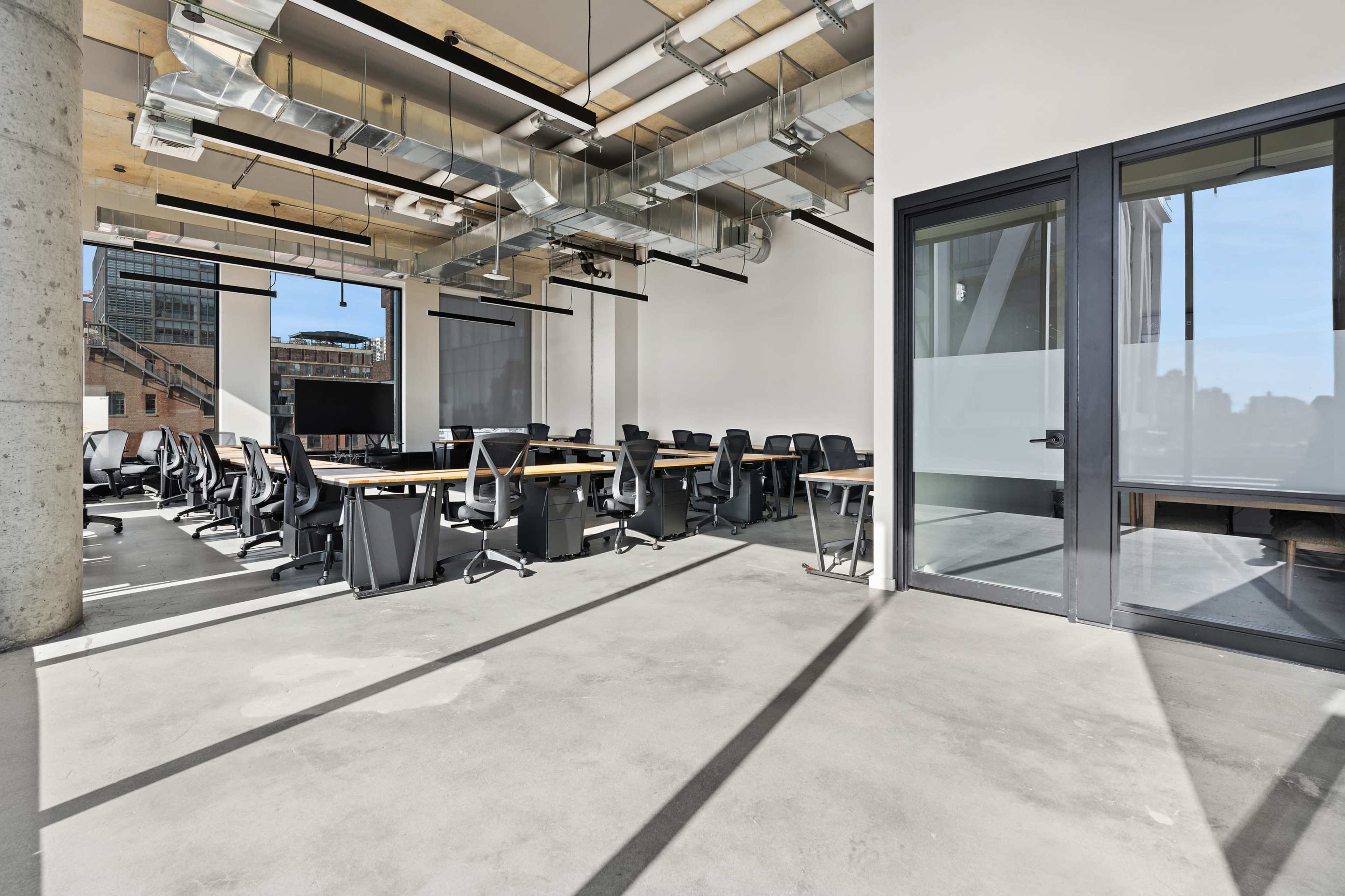 A spacious, modern conference room features long tables and ergonomic chairs, with large windows allowing natural light and a view of the city.