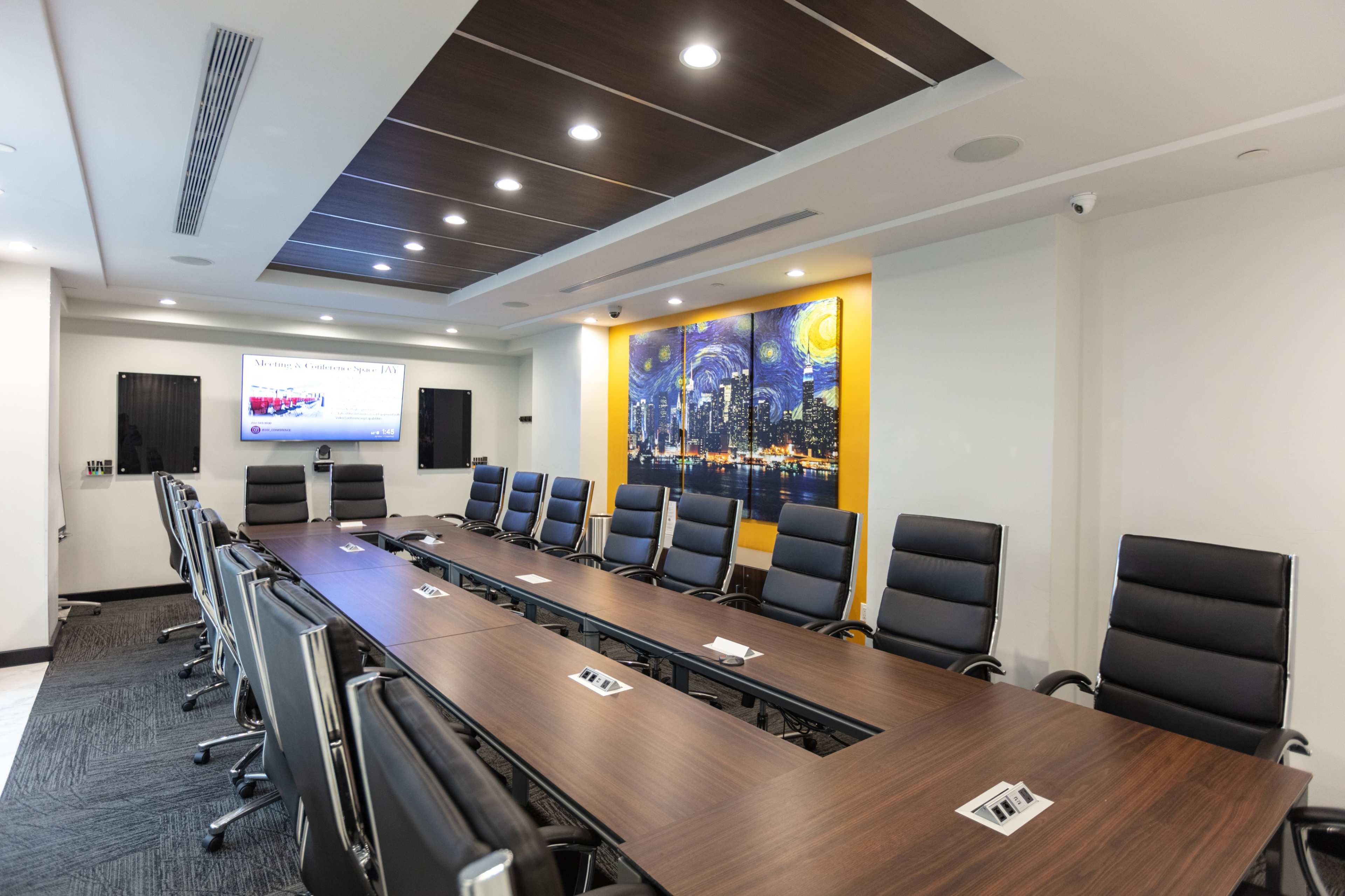 The image shows a modern conference room with a large wooden table surrounded by black office chairs and a wall featuring a cityscape mural.