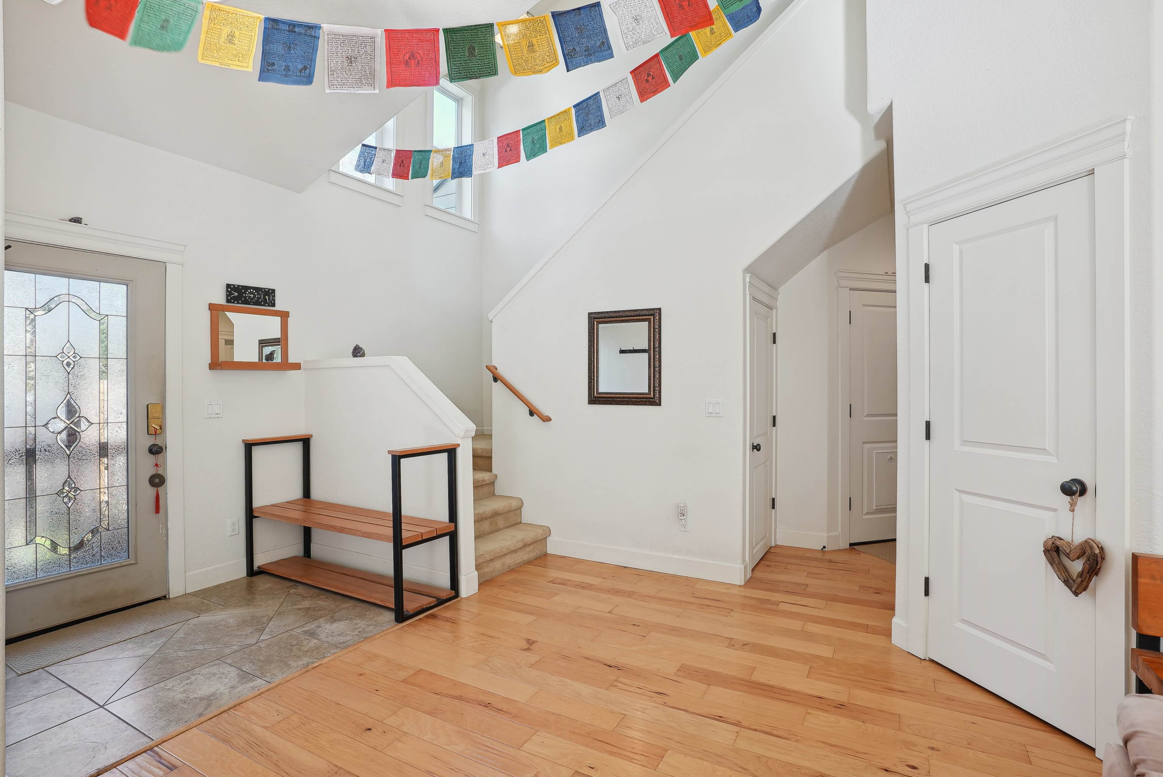 A bright entryway with a staircase, a wooden bench, and colorful decorative flags hanging from the ceiling.