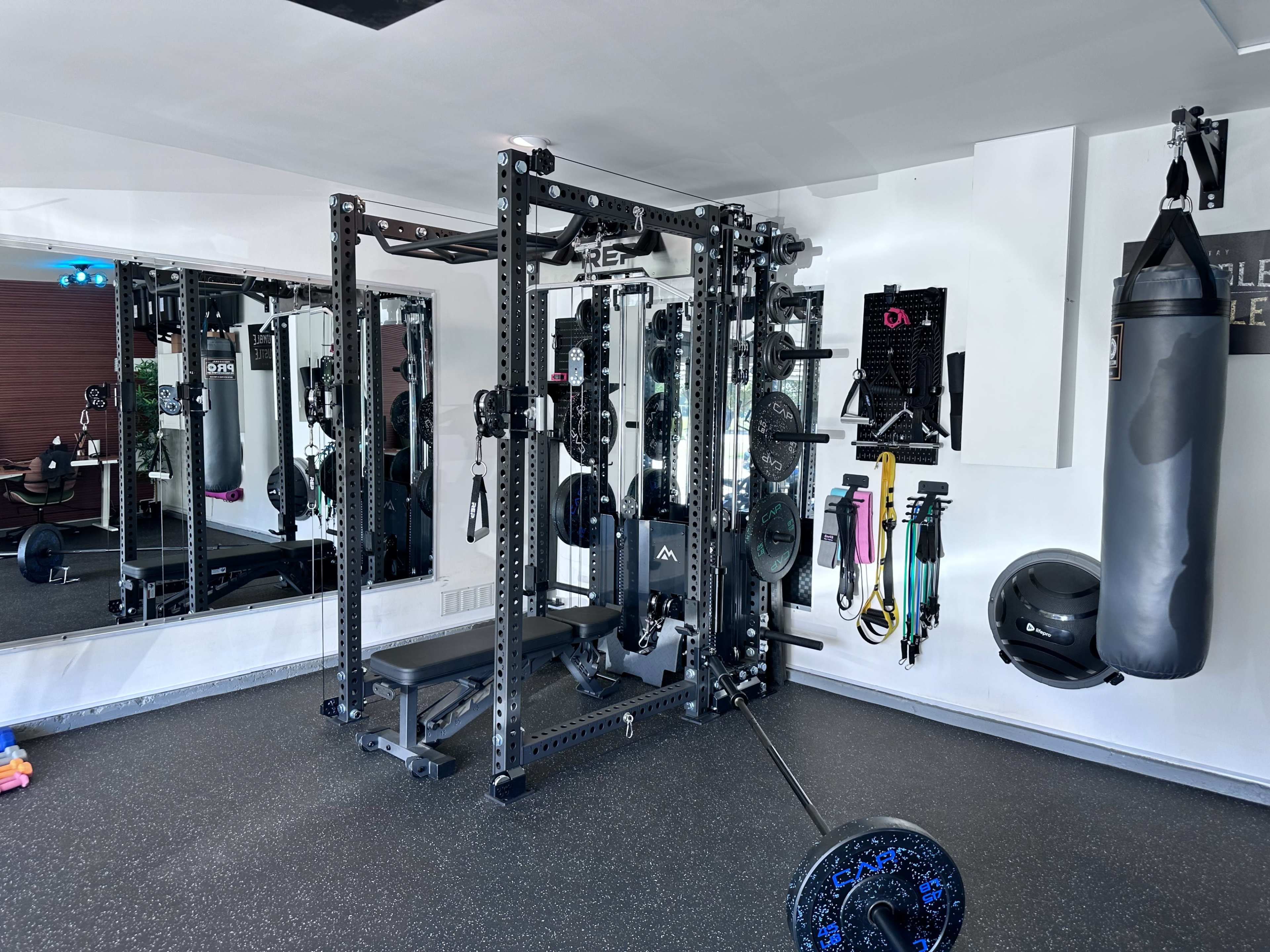 The image shows a home gym equipped with a weightlifting rack, a bench, various exercise accessories, and a punching bag.