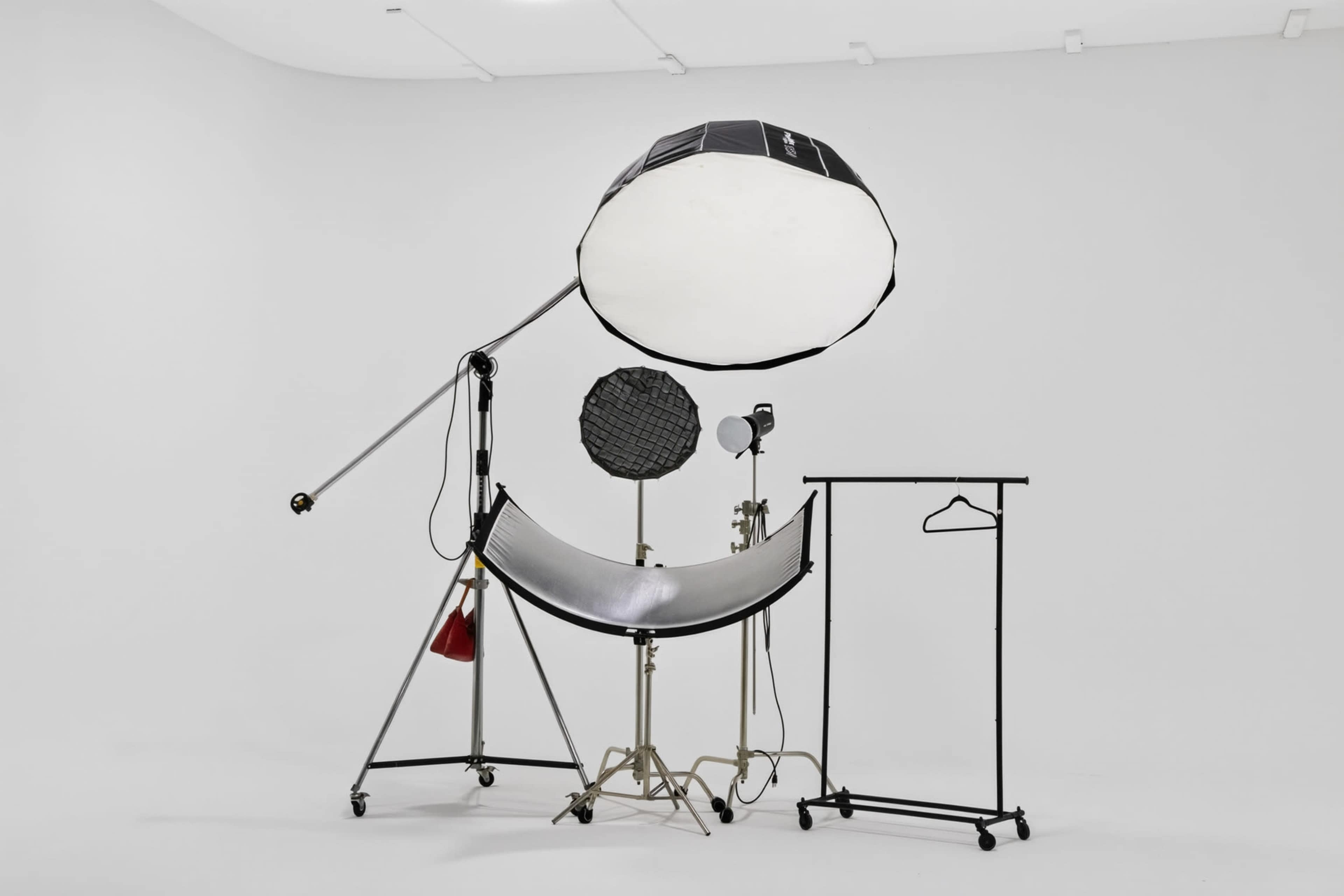 The image shows a photography setup featuring a large softbox, a reflector, and a hanging clothes rack against a plain white background.