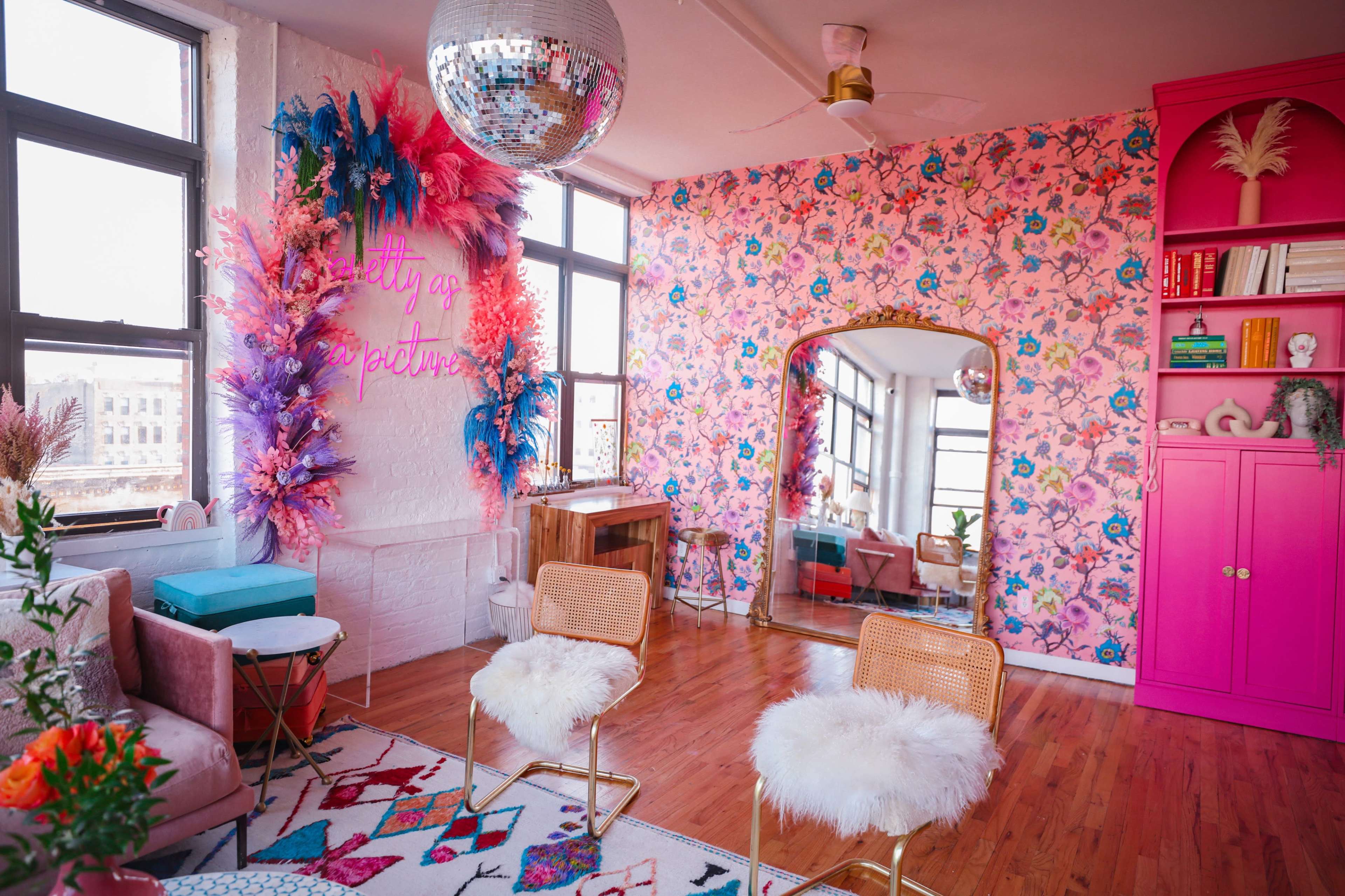 The room features colorful floral wallpaper, a large mirror, modern seating, and decorative elements including a disco ball and vibrant furnishings.