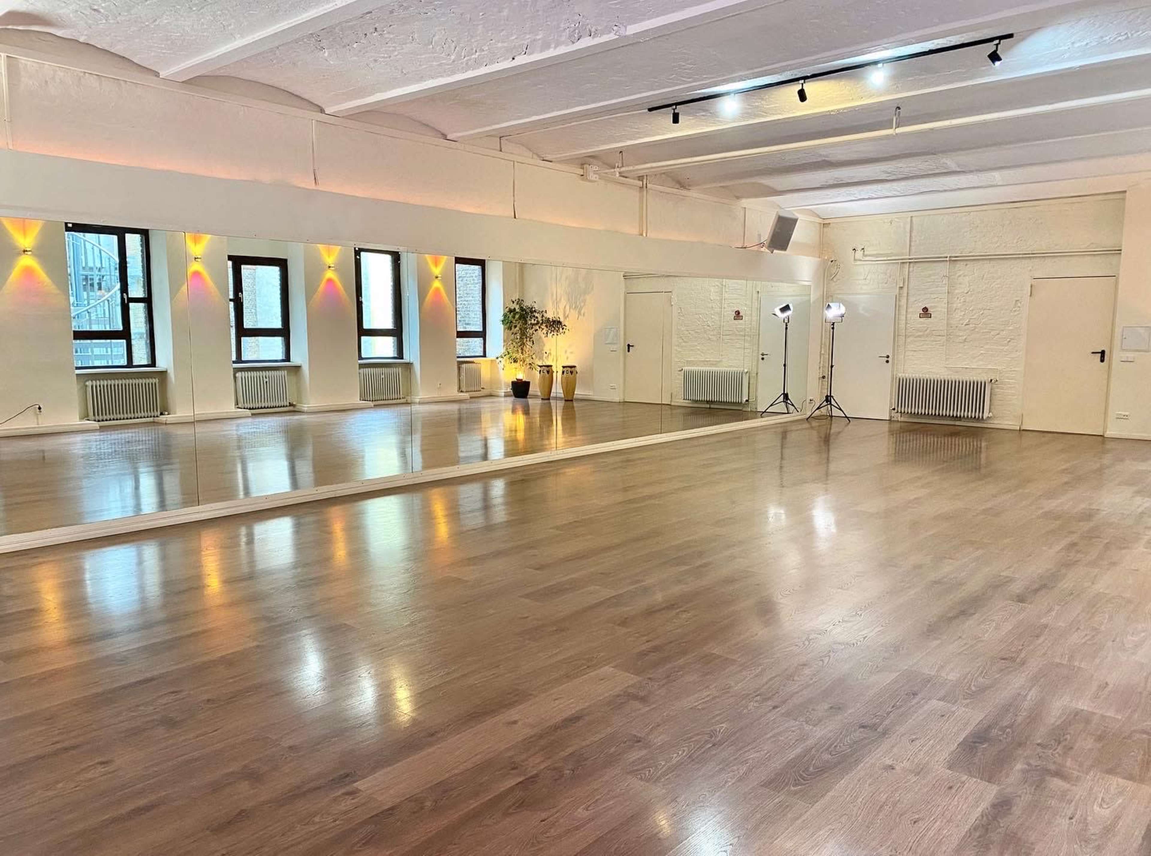 A spacious dance studio with a large mirror, wooden flooring, and soft ambient lighting.