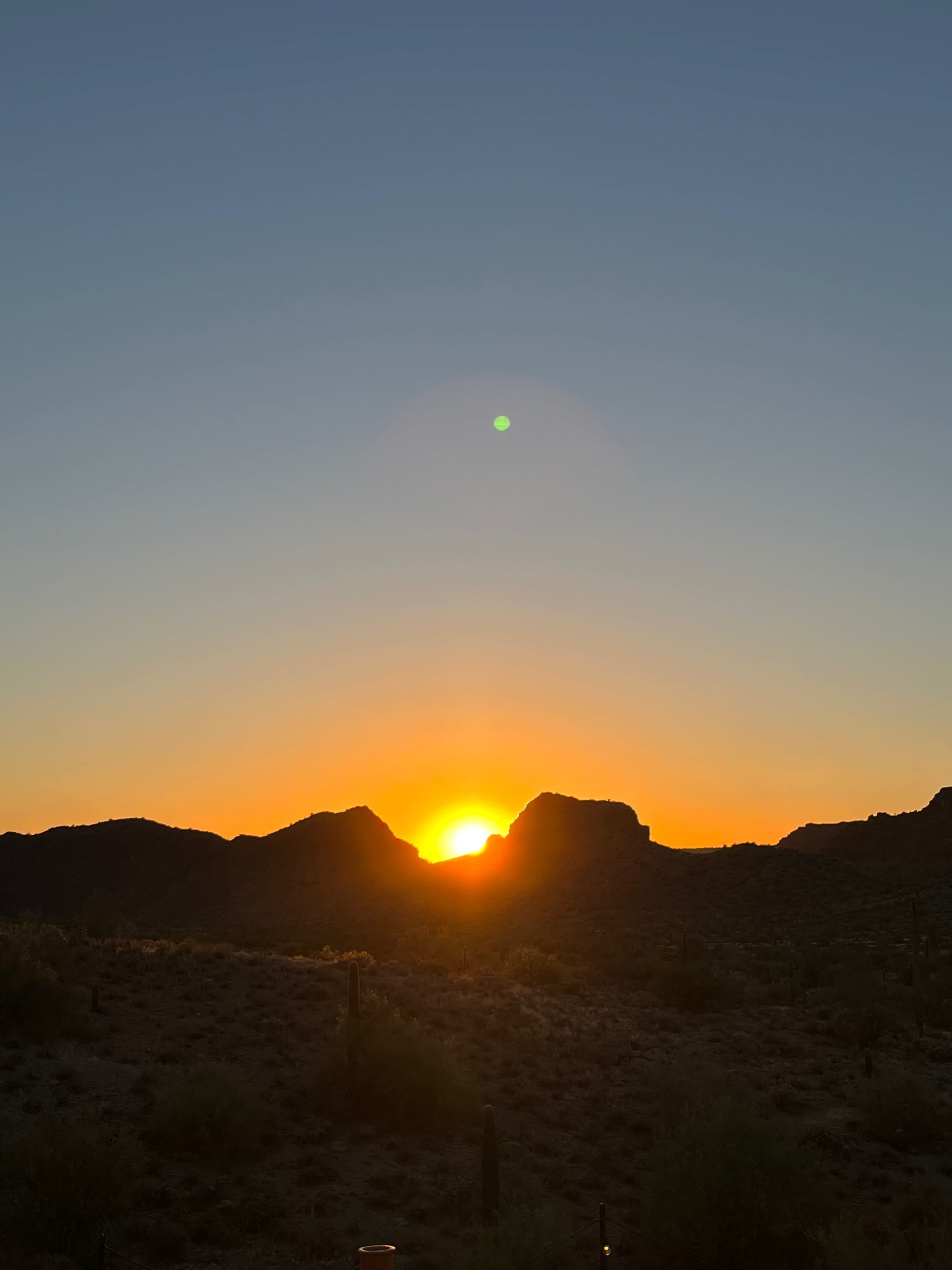 The sun sets behind rugged mountains in a desert landscape.