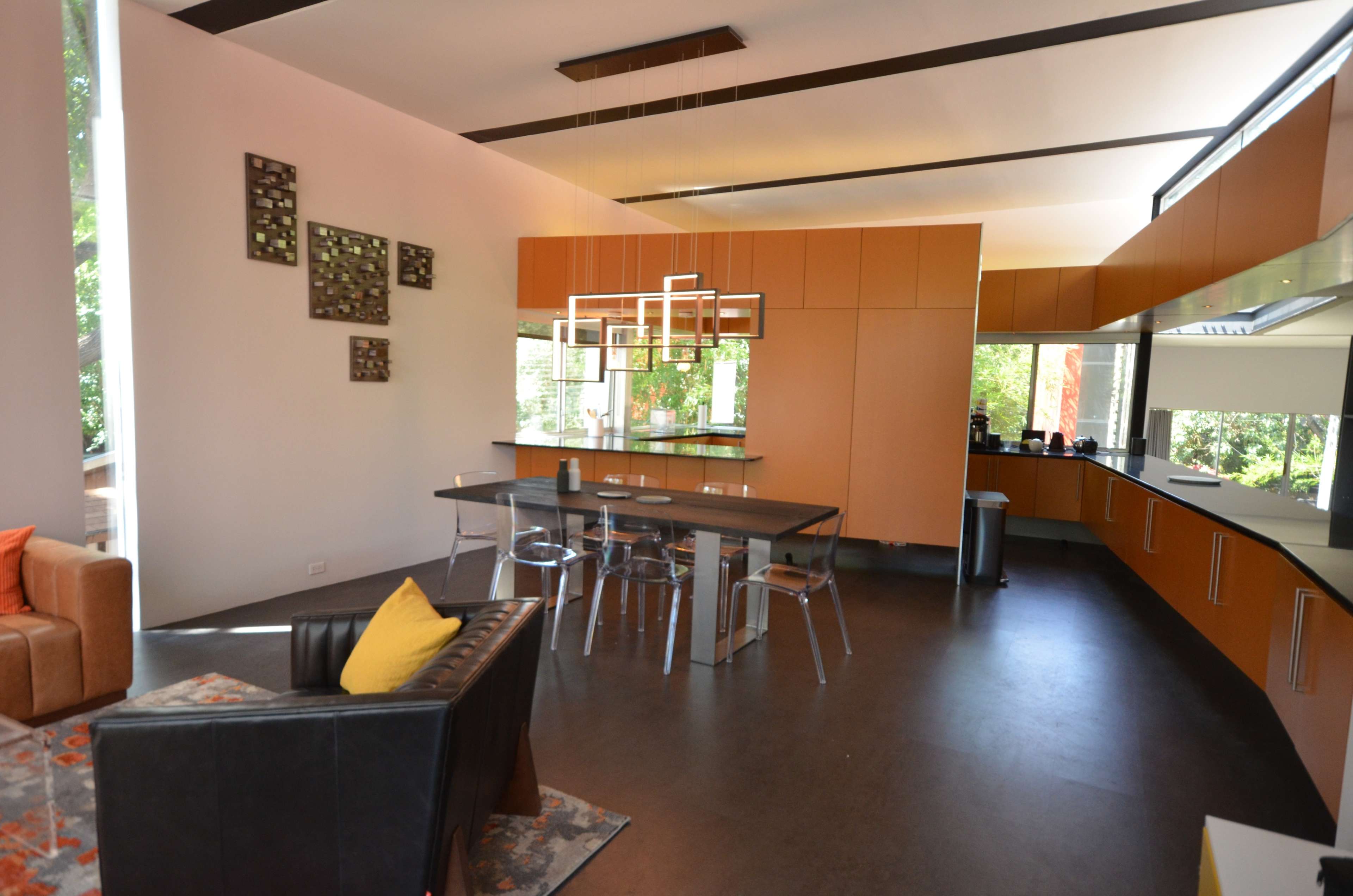 A modern kitchen and dining area with orange cabinetry, a sleek dining table, and clear dining chairs.