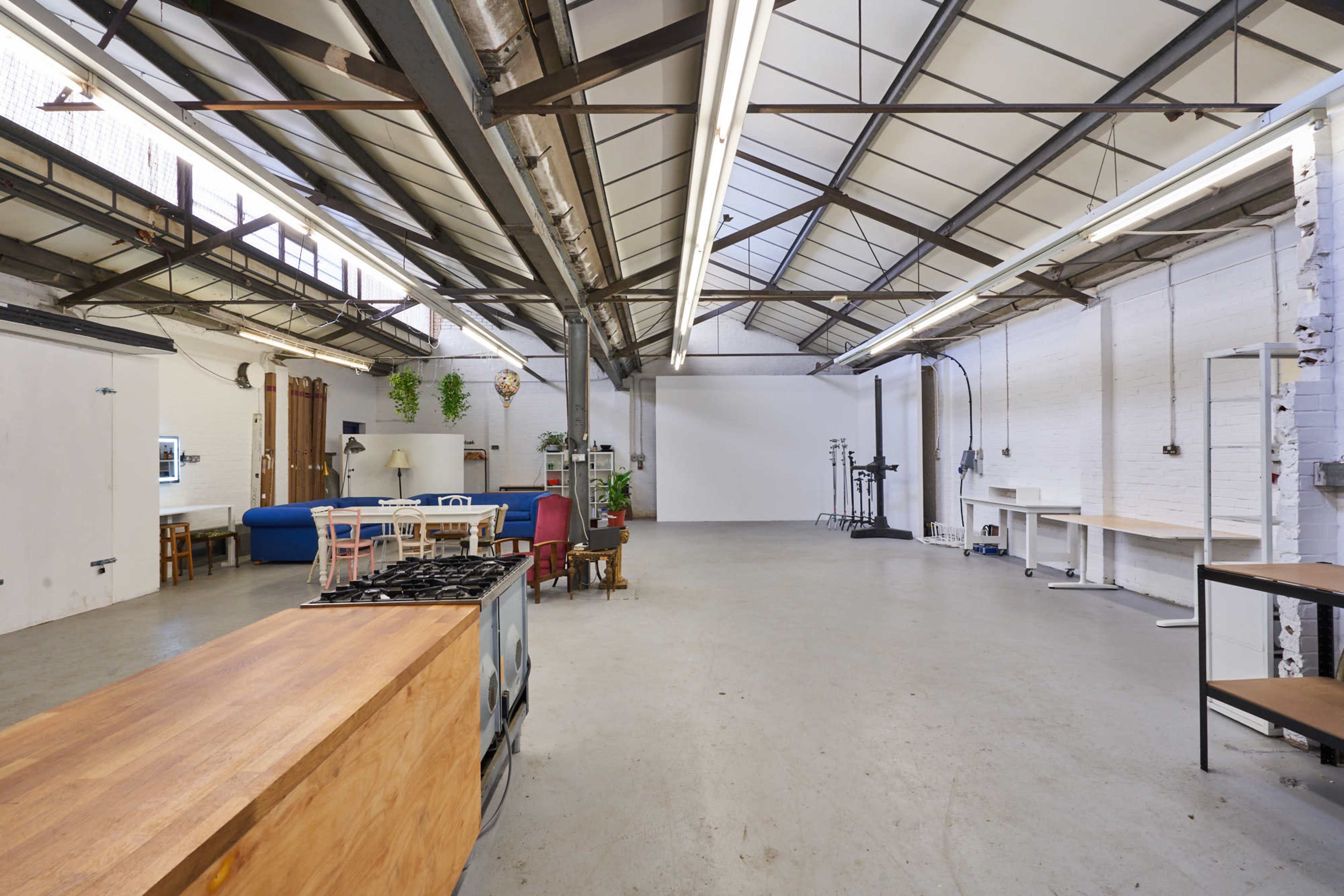 A spacious studio with high ceilings, featuring a kitchen area with a wooden counter, various seating arrangements, and a backdrop for photography.