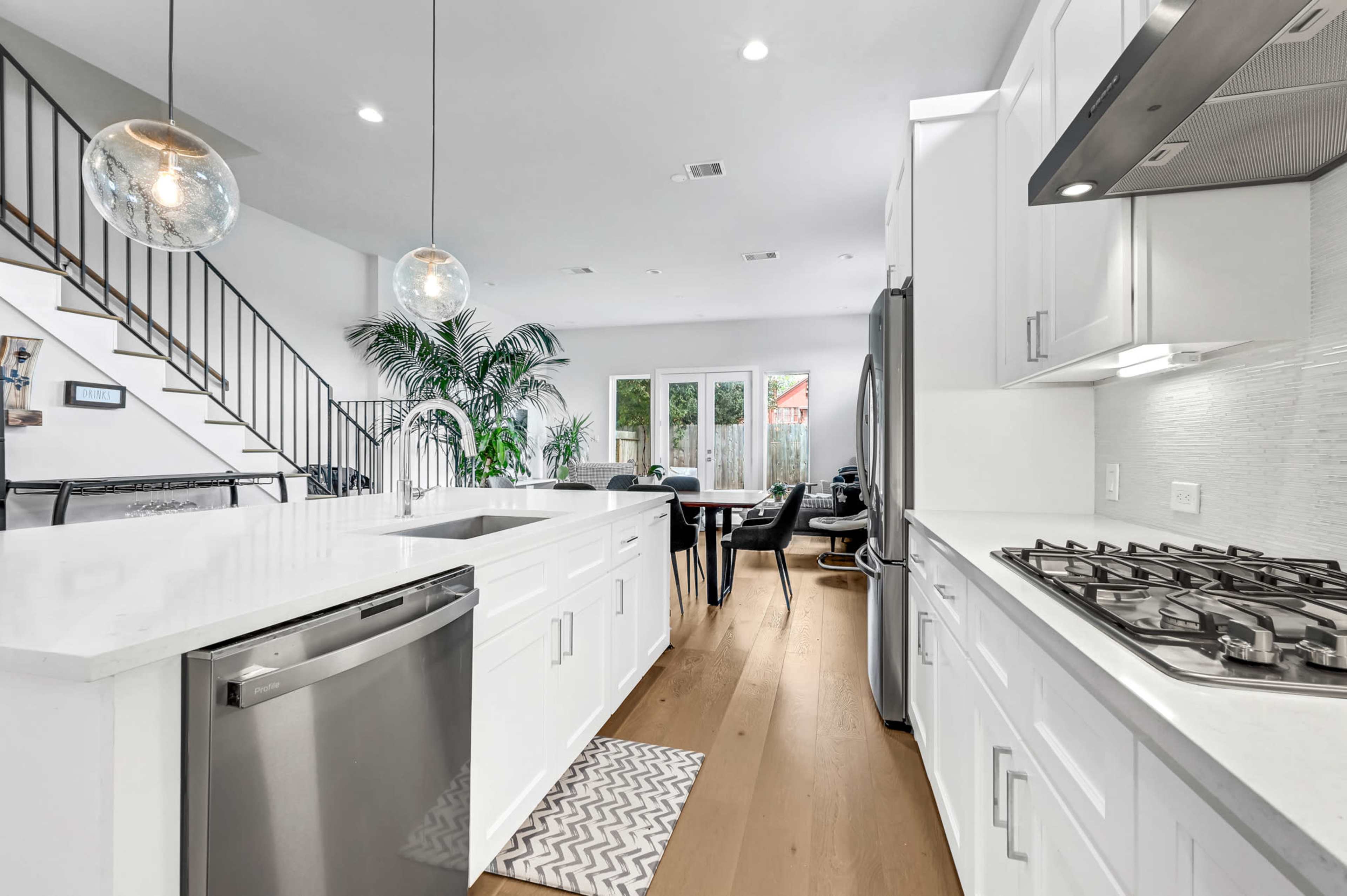 A modern kitchen features white cabinets, stainless steel appliances, and a large island with pendant lighting, leading to a dining area with a glass door.