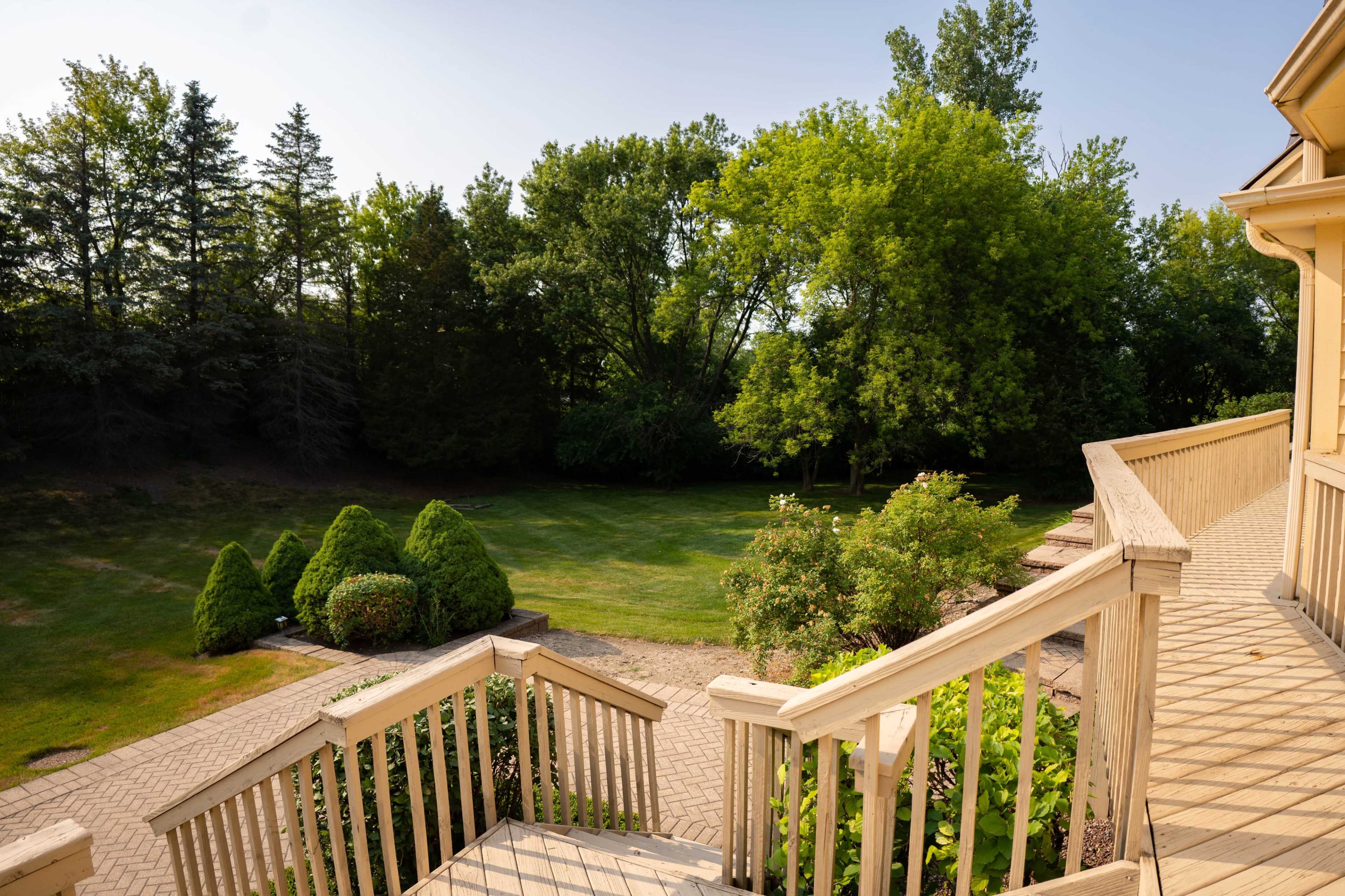 A wooden deck with a staircase leading down to a manicured lawn surrounded by trees.