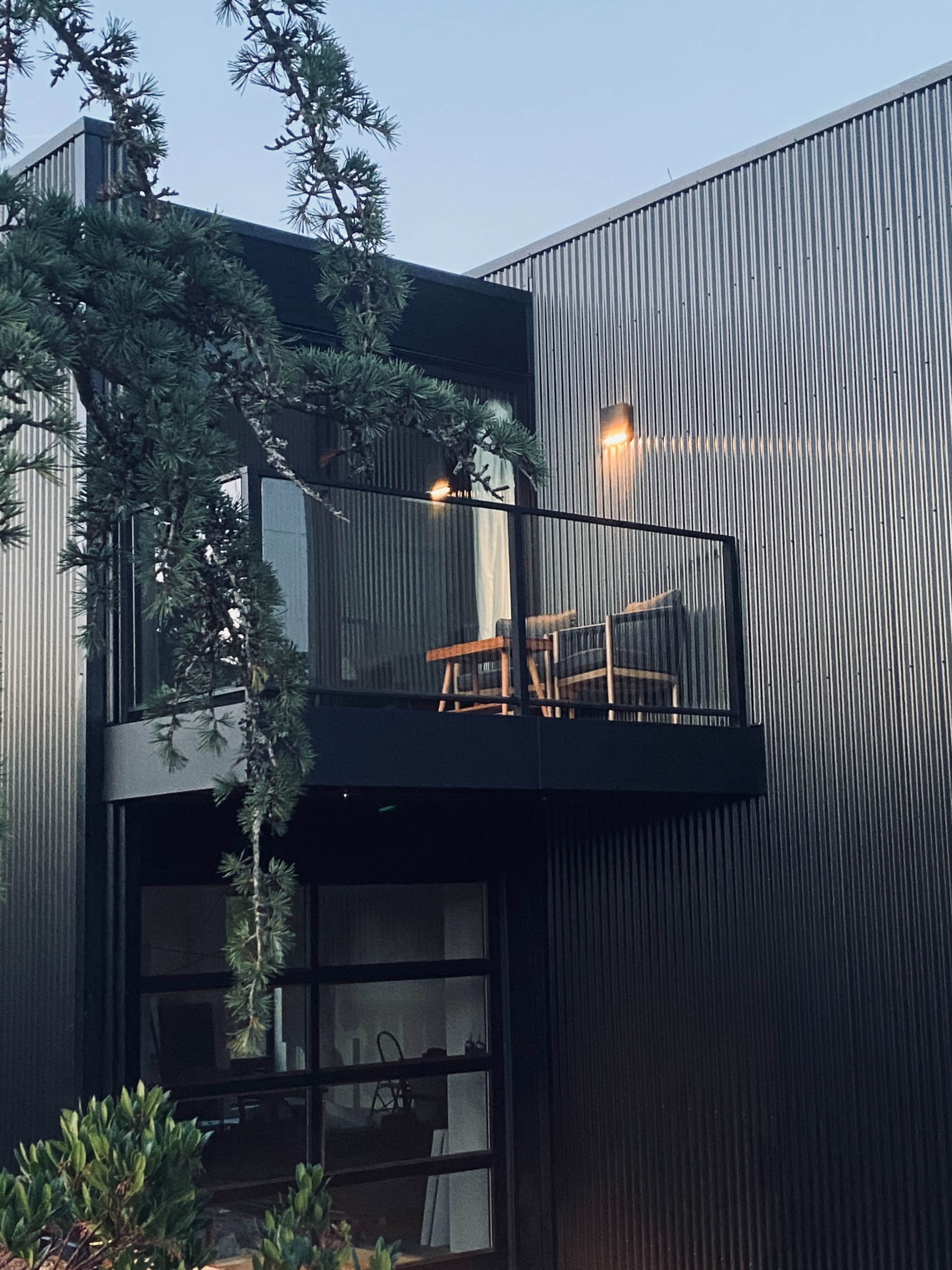A modern building features a balcony with two chairs overlooking a lush green area.