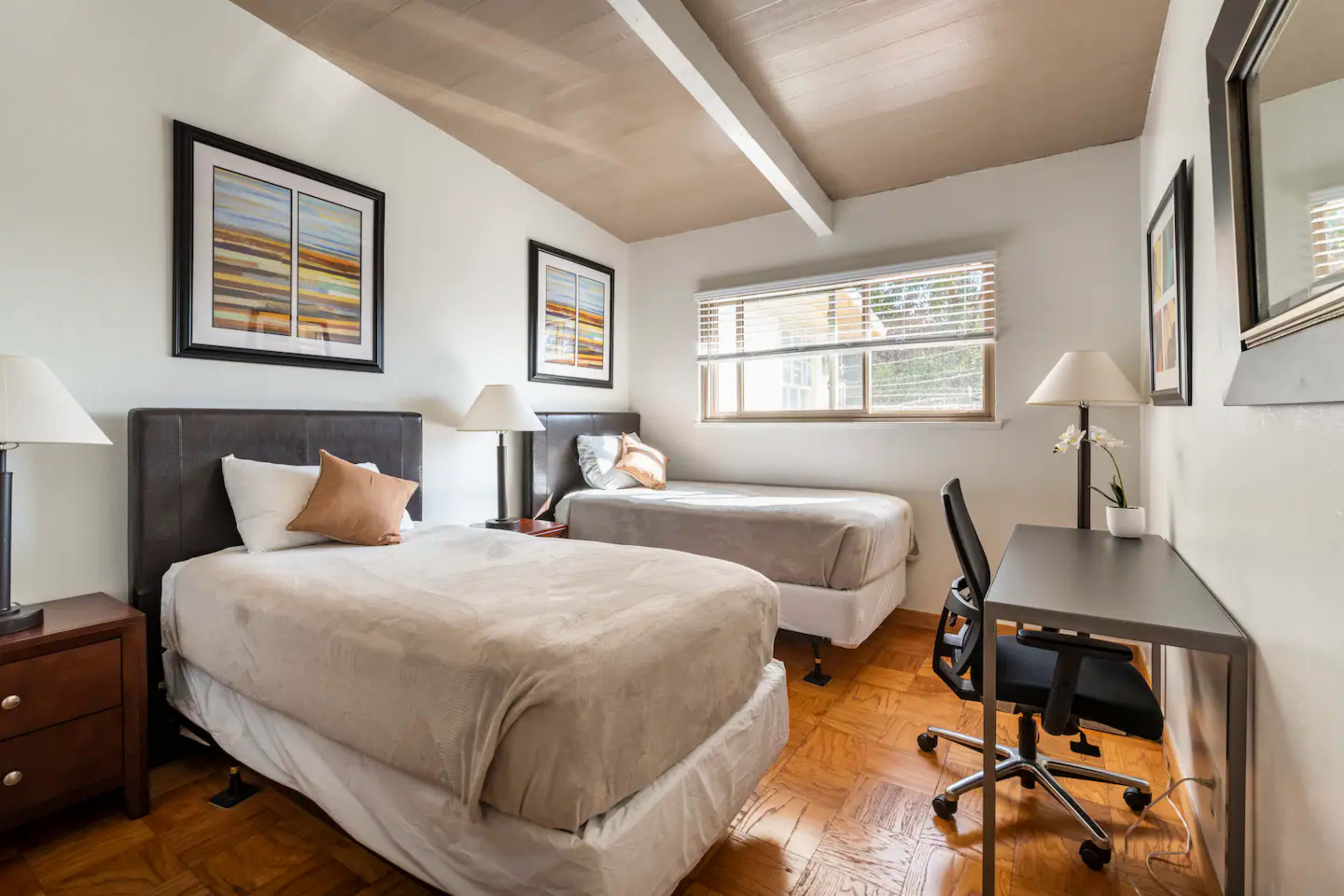 A bedroom with two twin beds, a desk and chair, and artwork on the walls.