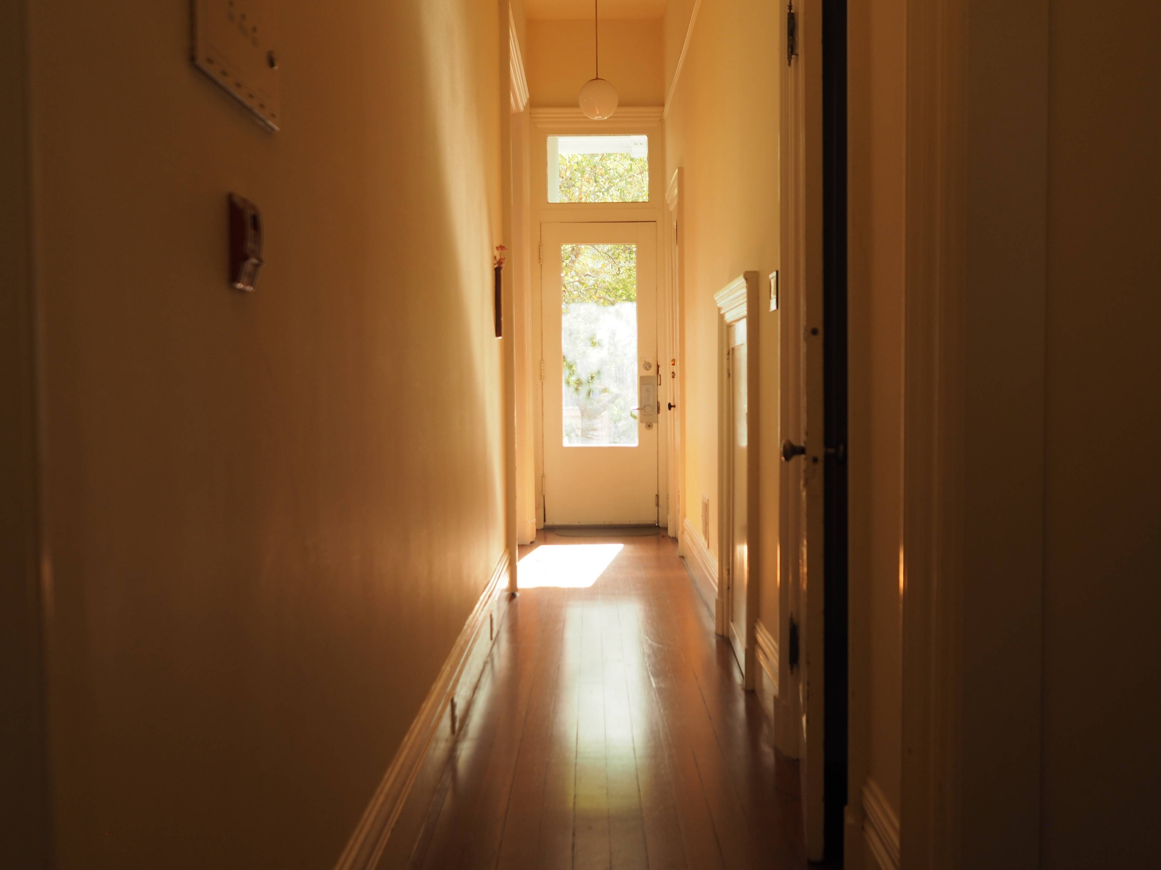A long hallway with wooden flooring leads to a door at the far end, illuminated by natural light.