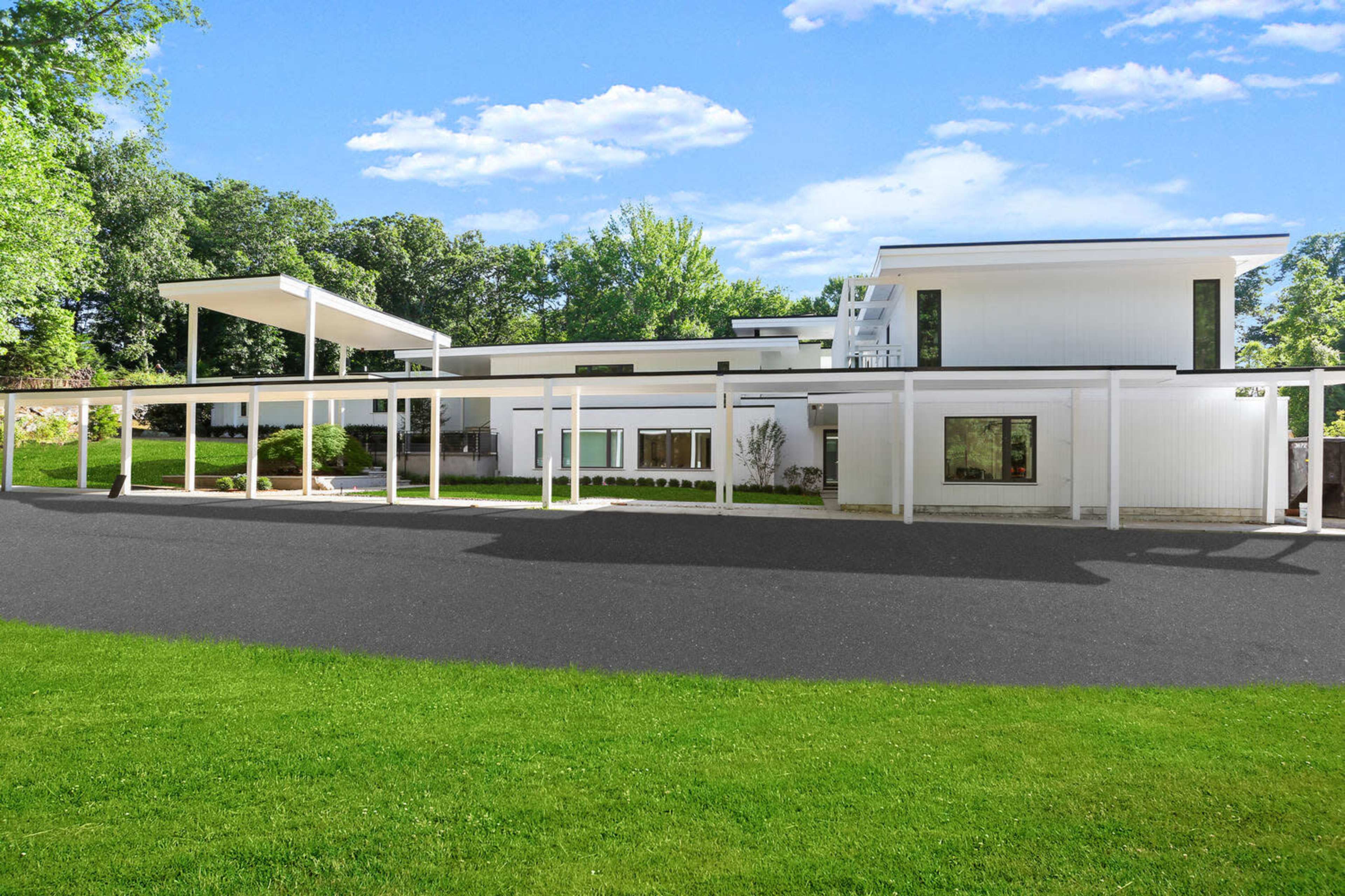 The image shows a modern, white, two-story building with large windows, surrounded by a green lawn and a paved driveway.