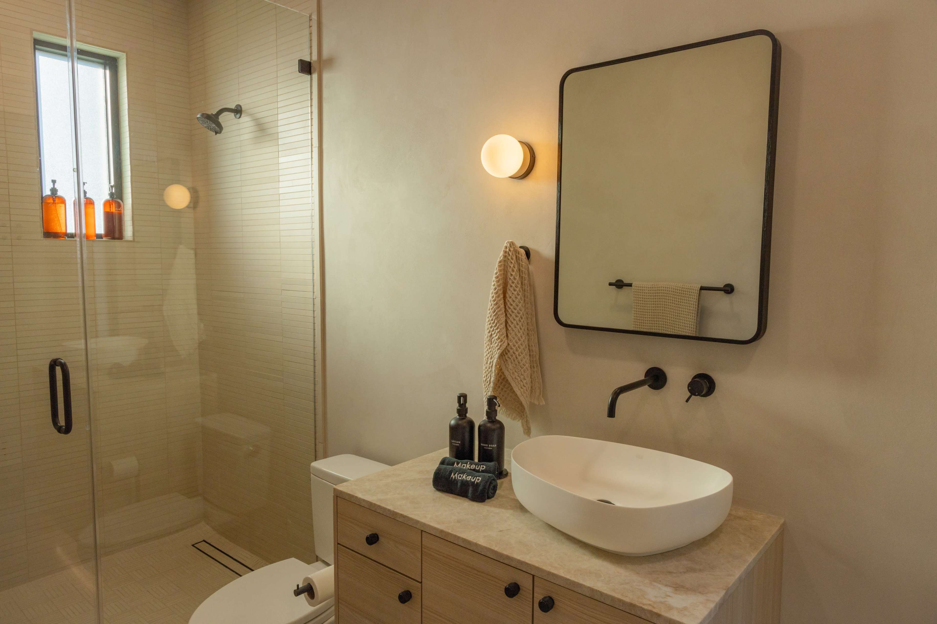 A modern bathroom featuring a glass shower, a wall-mounted sink with a stone countertop, and a large mirror above it.