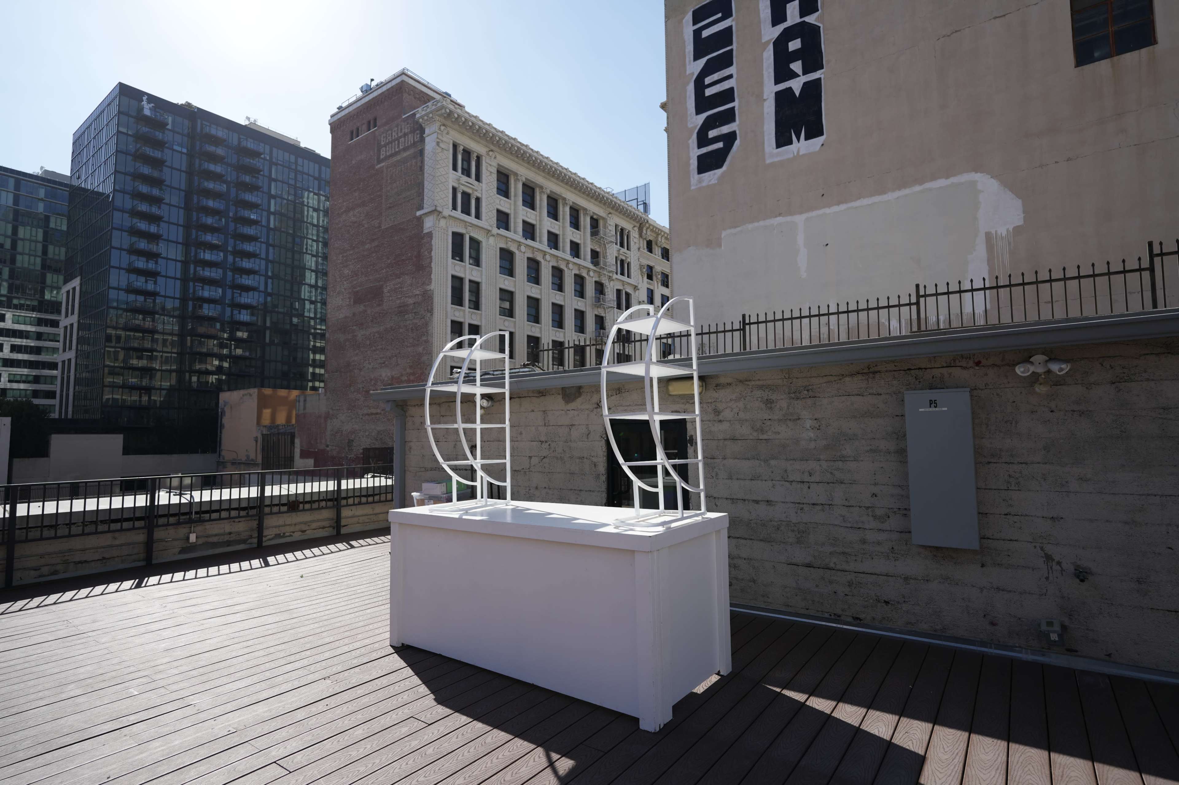 A white, modern structure stands on a wooden deck surrounded by tall buildings and brick architecture.