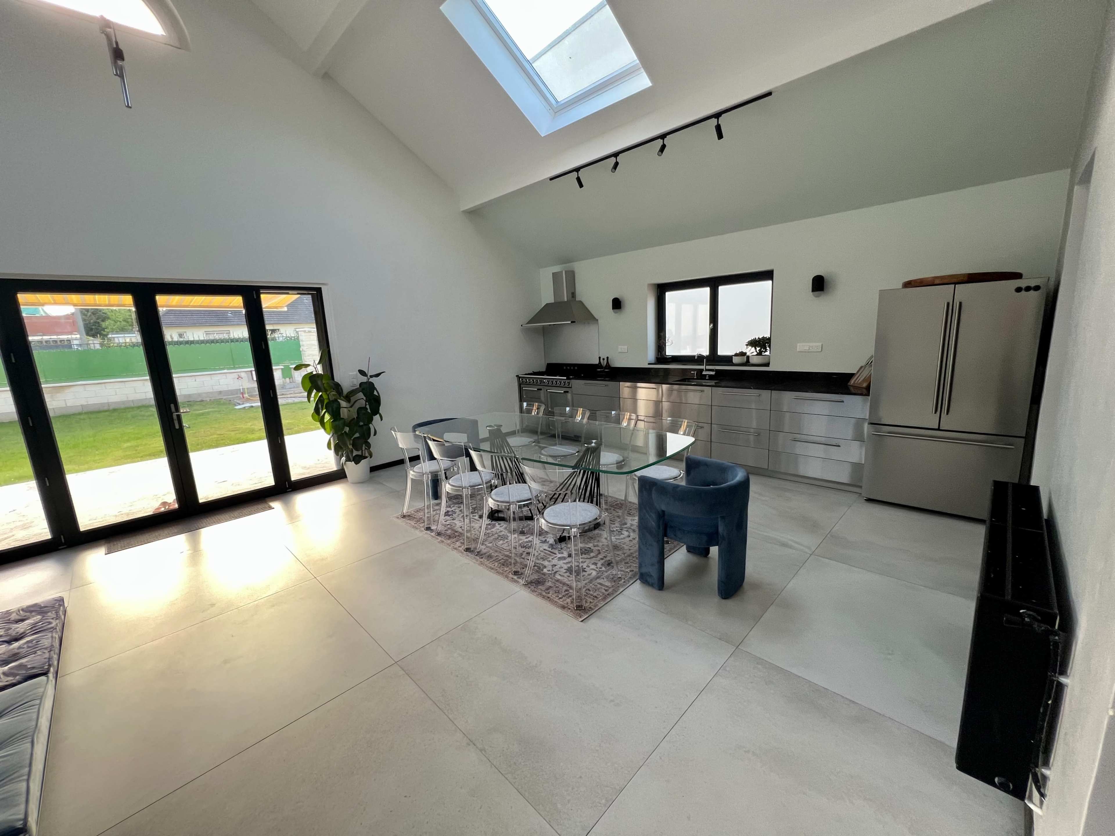 A bright, modern kitchen and dining area with a glass table, stainless steel appliances, and large windows that overlook a grassy outdoor space.