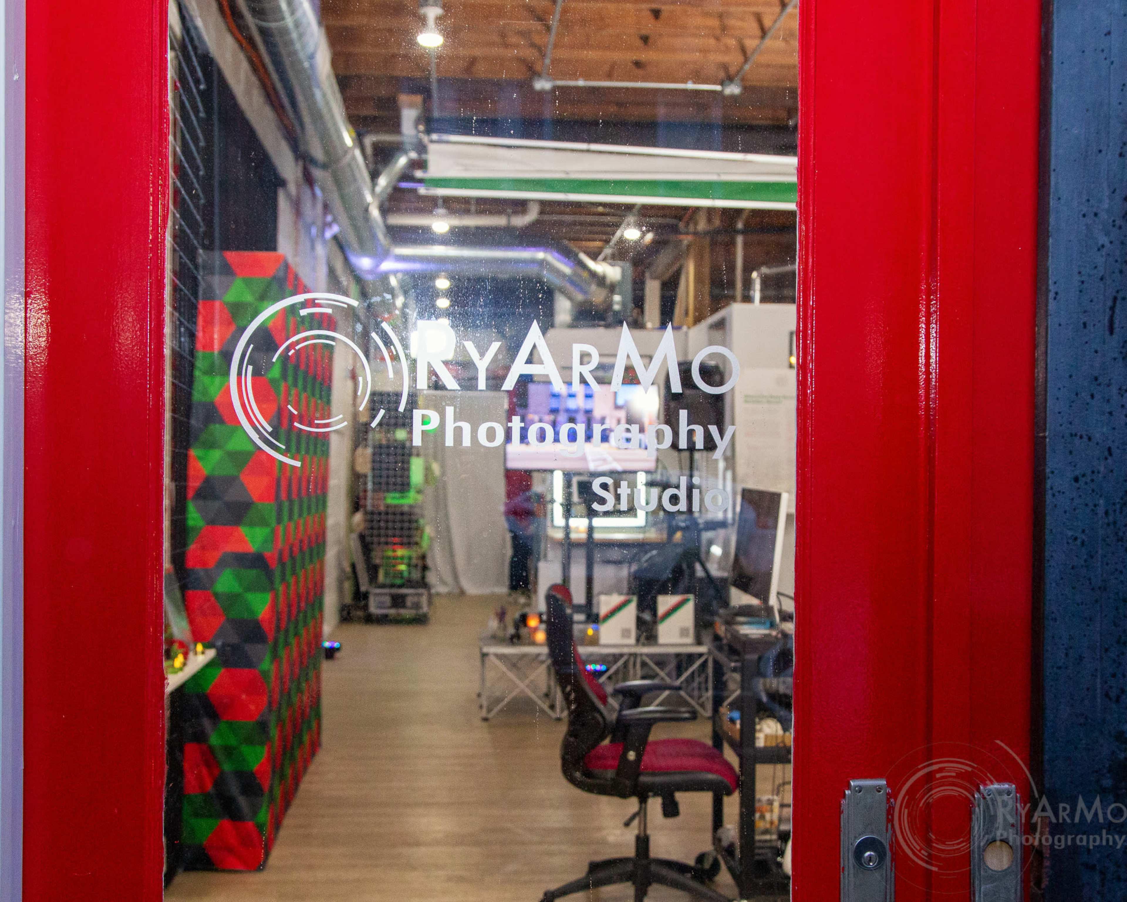 The image shows a brightly lit photography studio with a red door, featuring equipment and colorful backdrops visible through the glass.