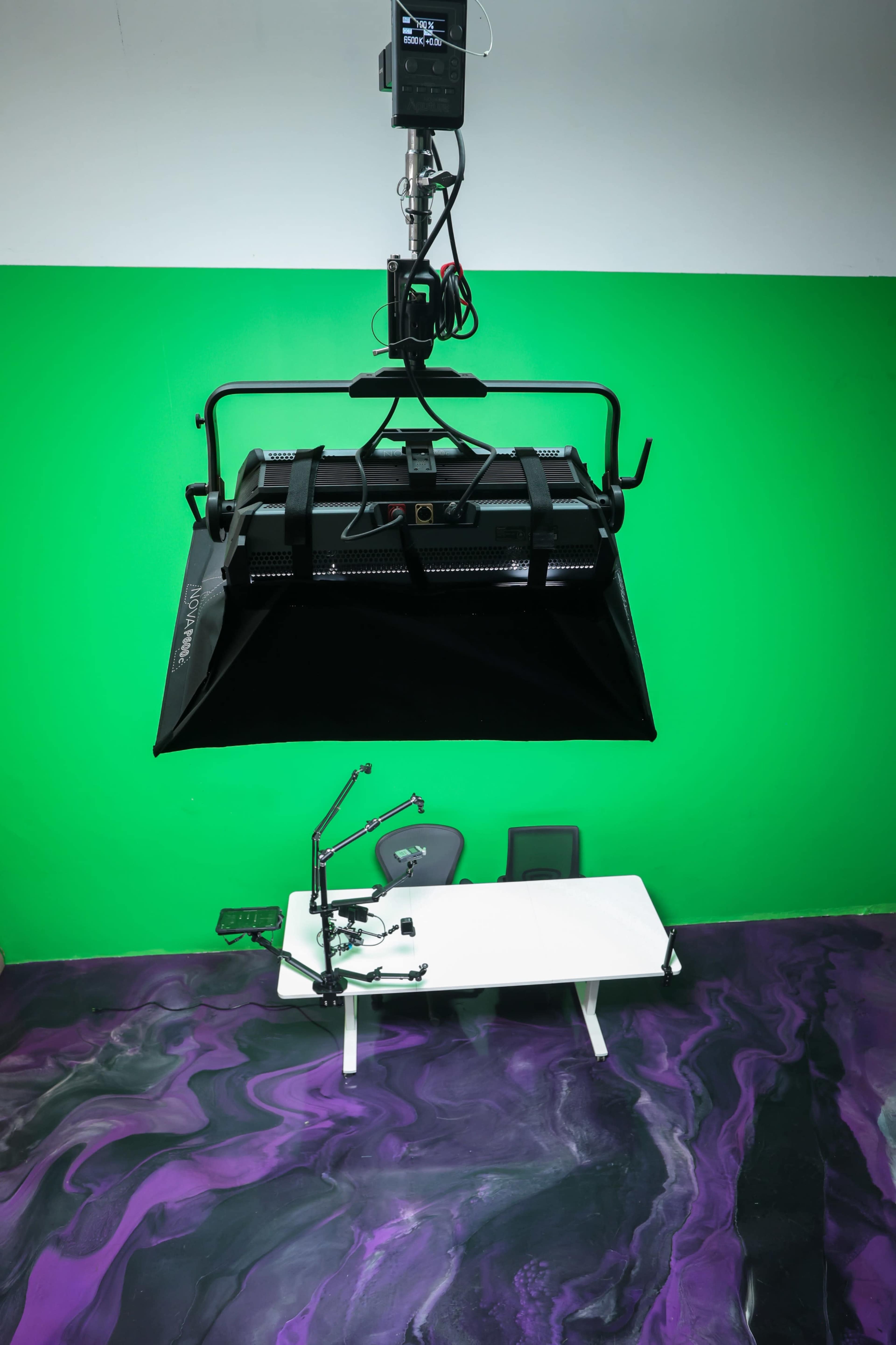 The image shows a studio setup with a green wall, a spotlight positioned above a white table, and two chairs on a purple marbled floor.