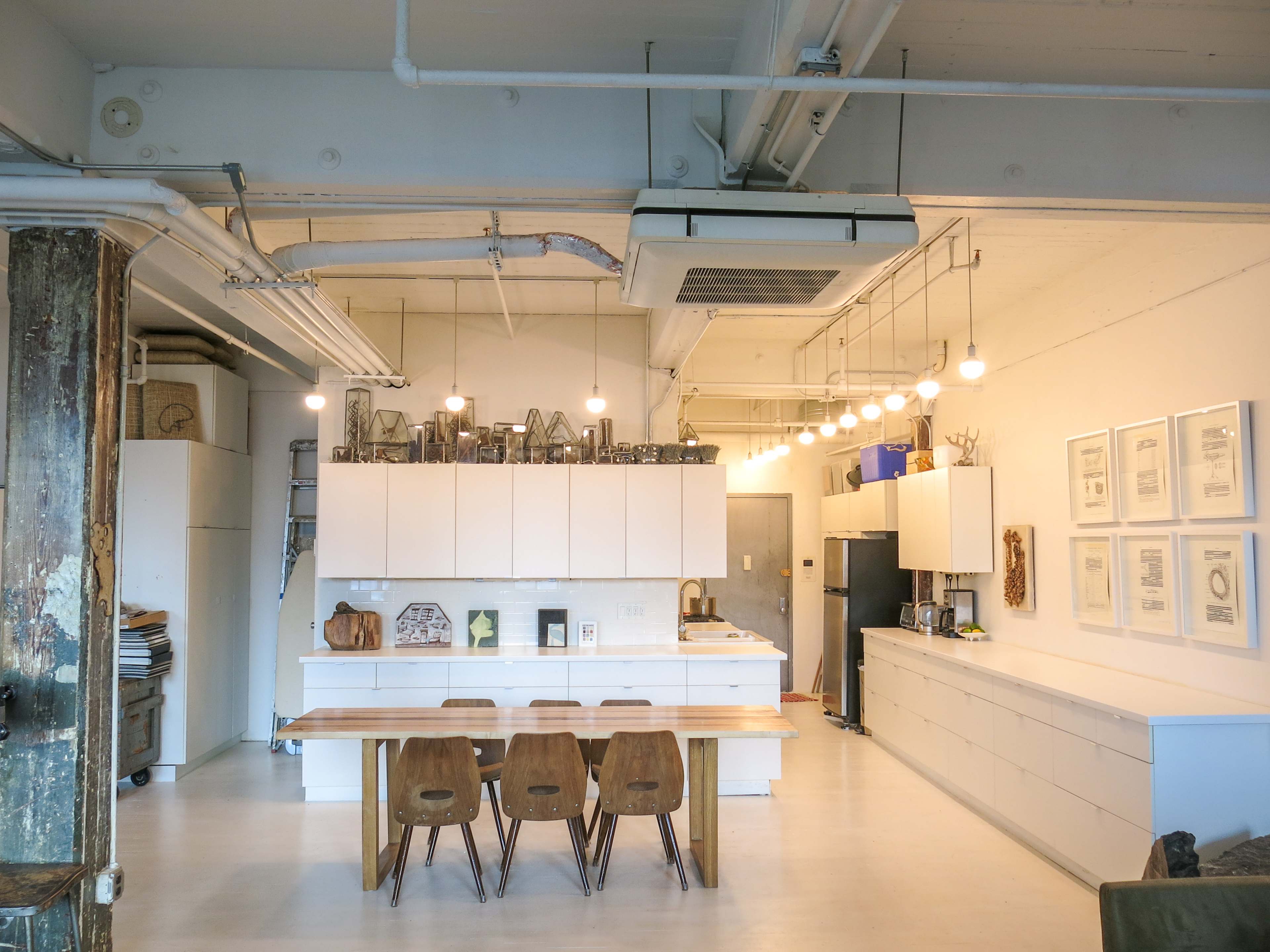 A modern kitchen features white cabinetry, wooden dining chairs, and pendant lighting above a long table.