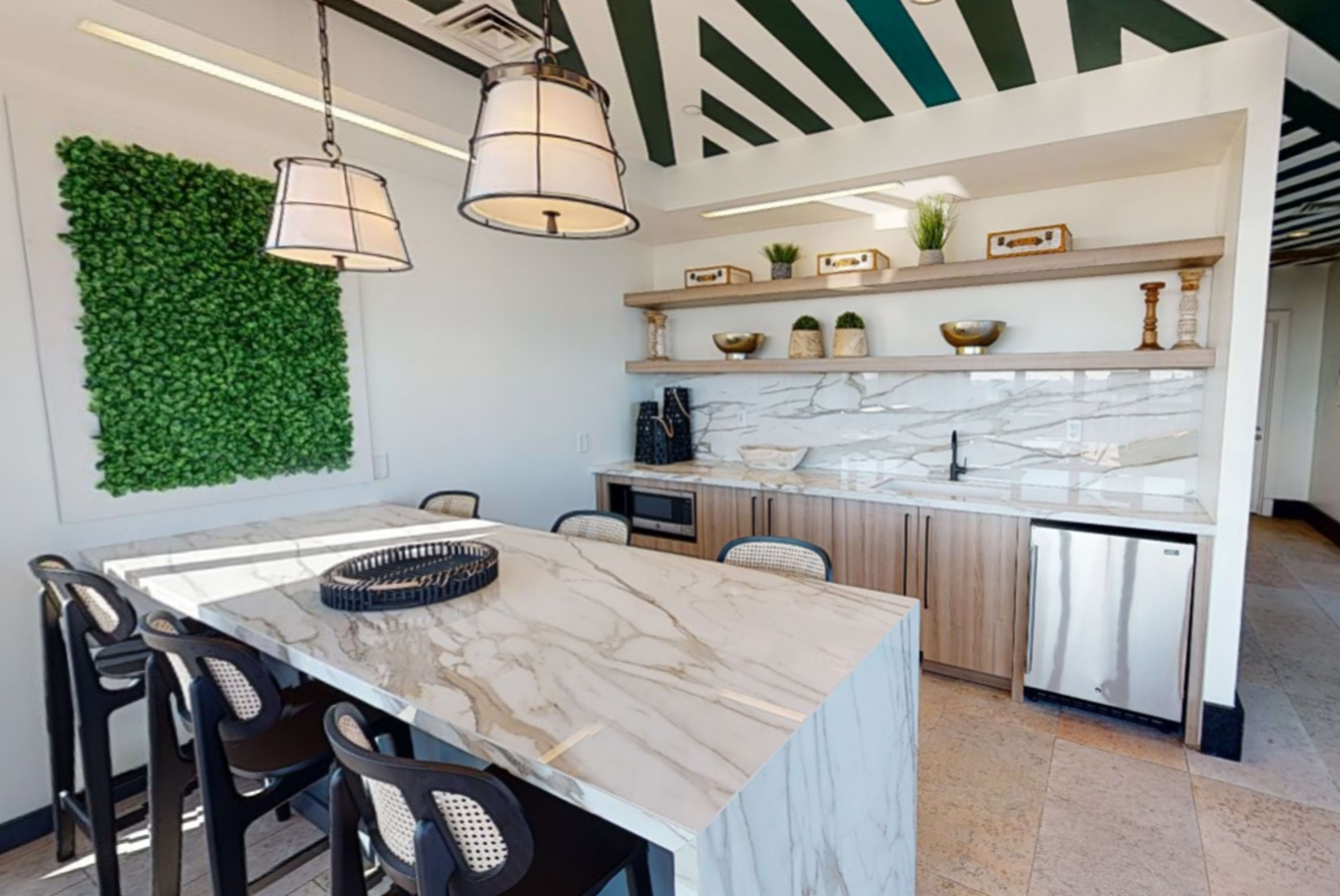 A modern kitchen space featuring a marble countertop island with bar seating, a green wall panel, and wooden shelves displaying decorative items.