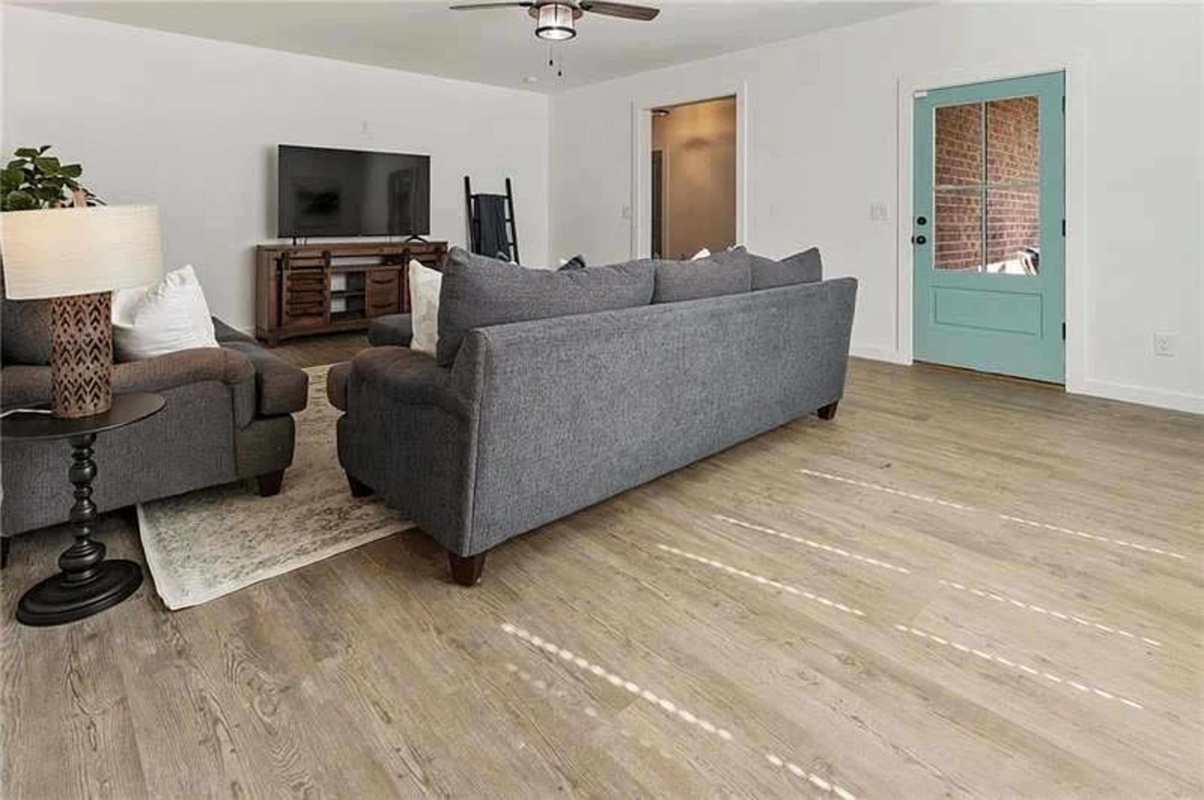 A living room features a gray couch and chairs, a television on a wooden stand, and a blue door leading outside.