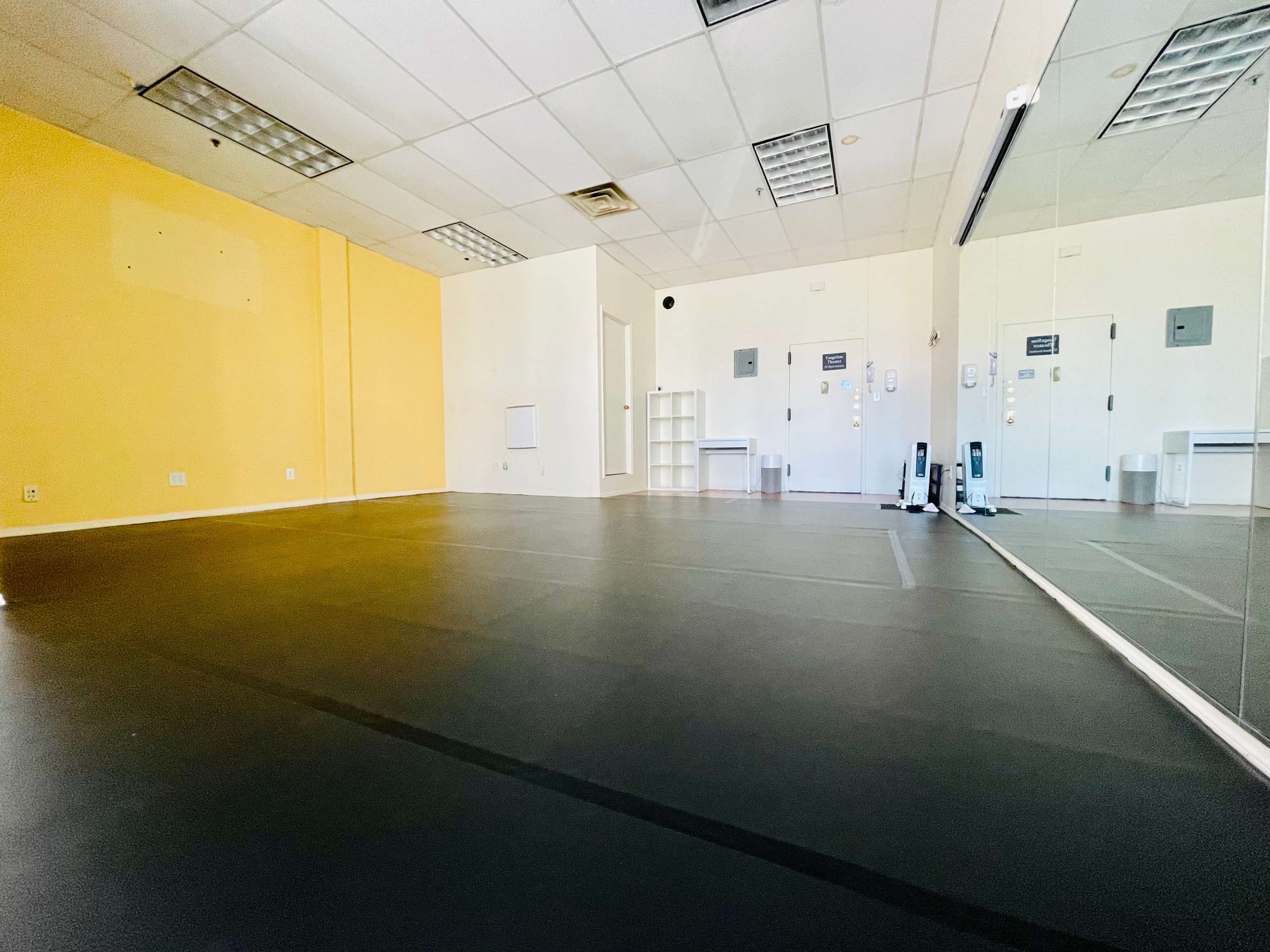 A spacious room with black flooring, yellow walls, and large mirrors on one side.