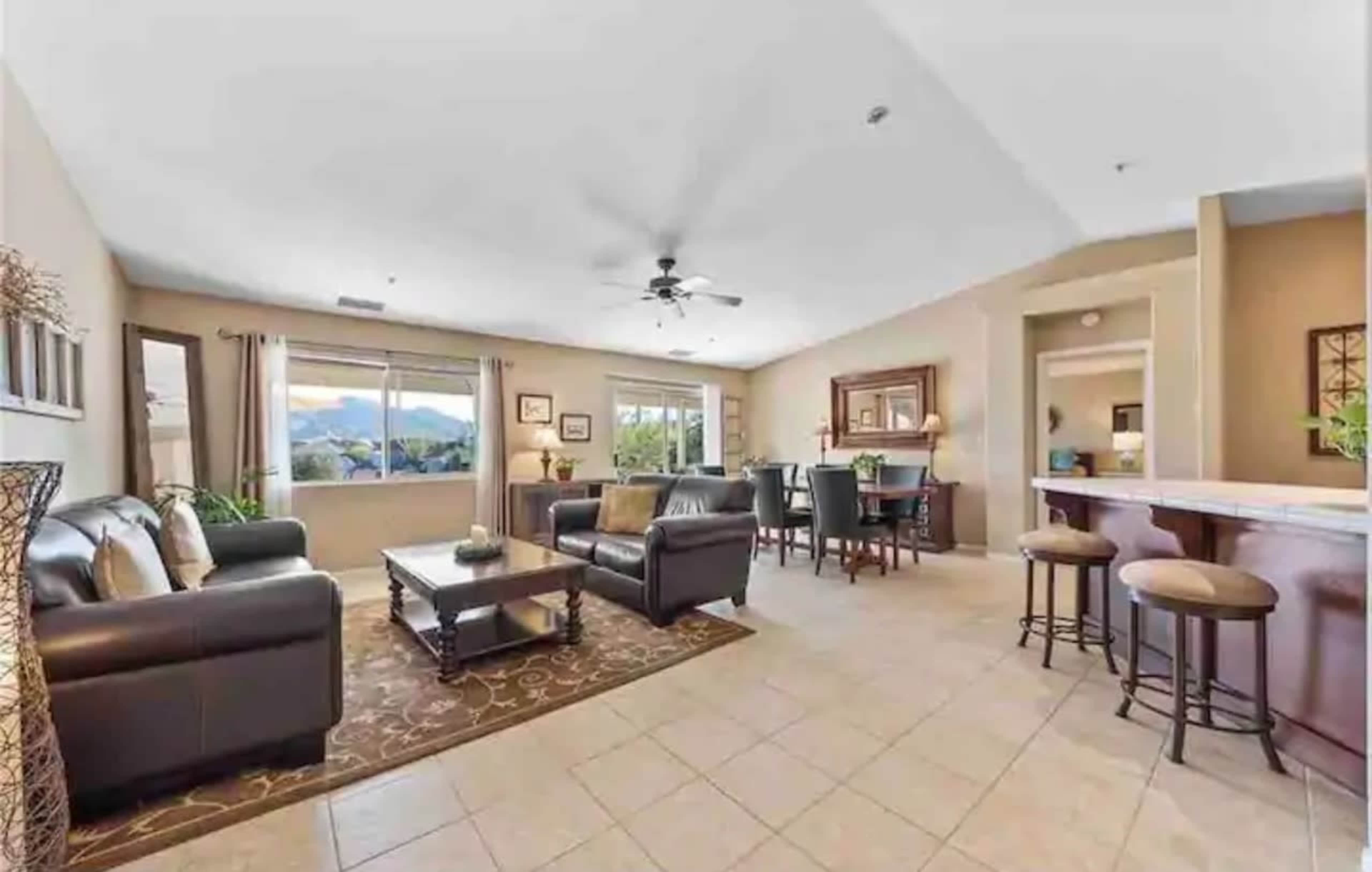 A spacious living room with a seating area, a dining space, and a kitchen bar, featuring large windows that offer a view of the mountains.