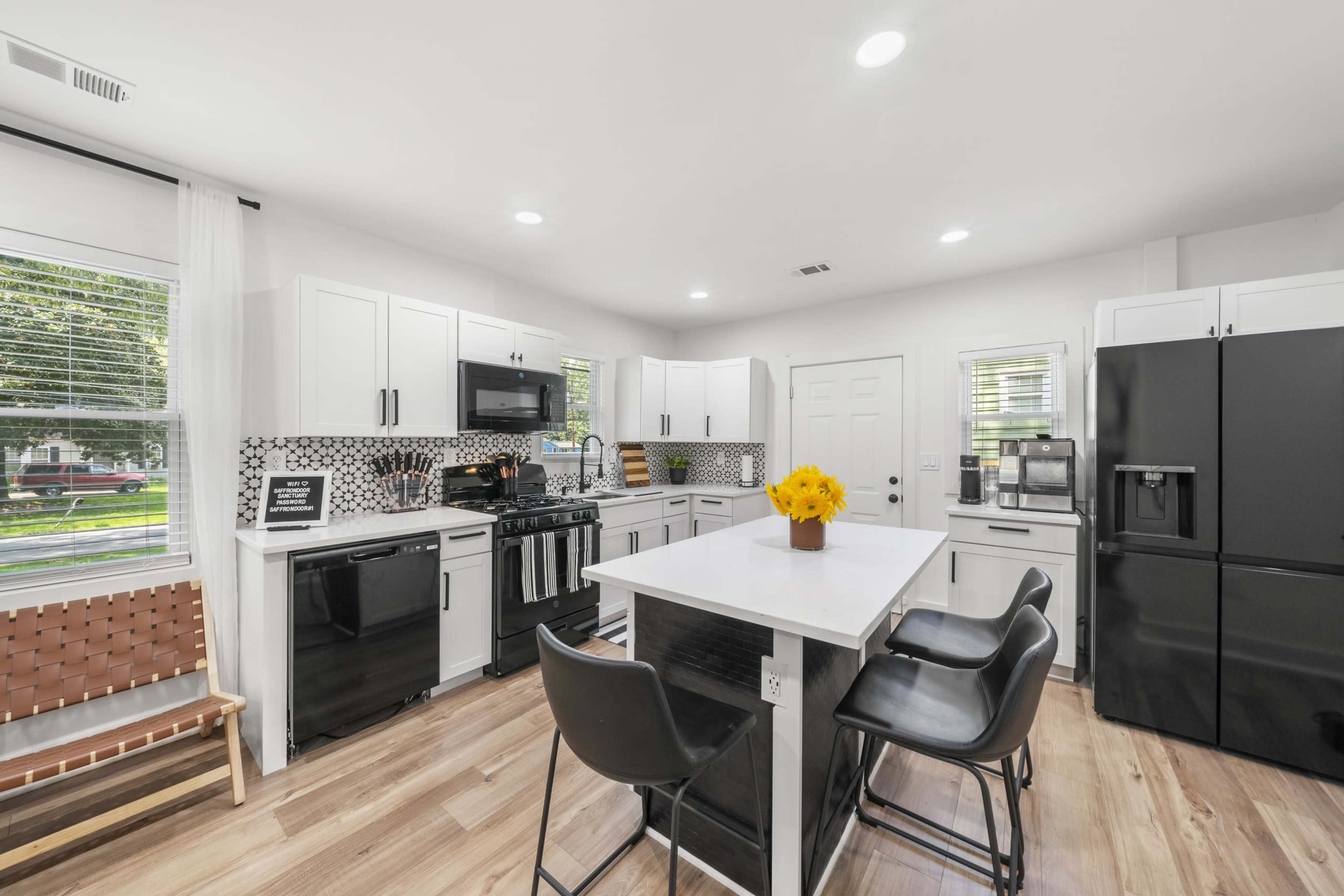 A modern kitchen with white cabinets, a black refrigerator, and a central island with seating and a vase of yellow flowers.