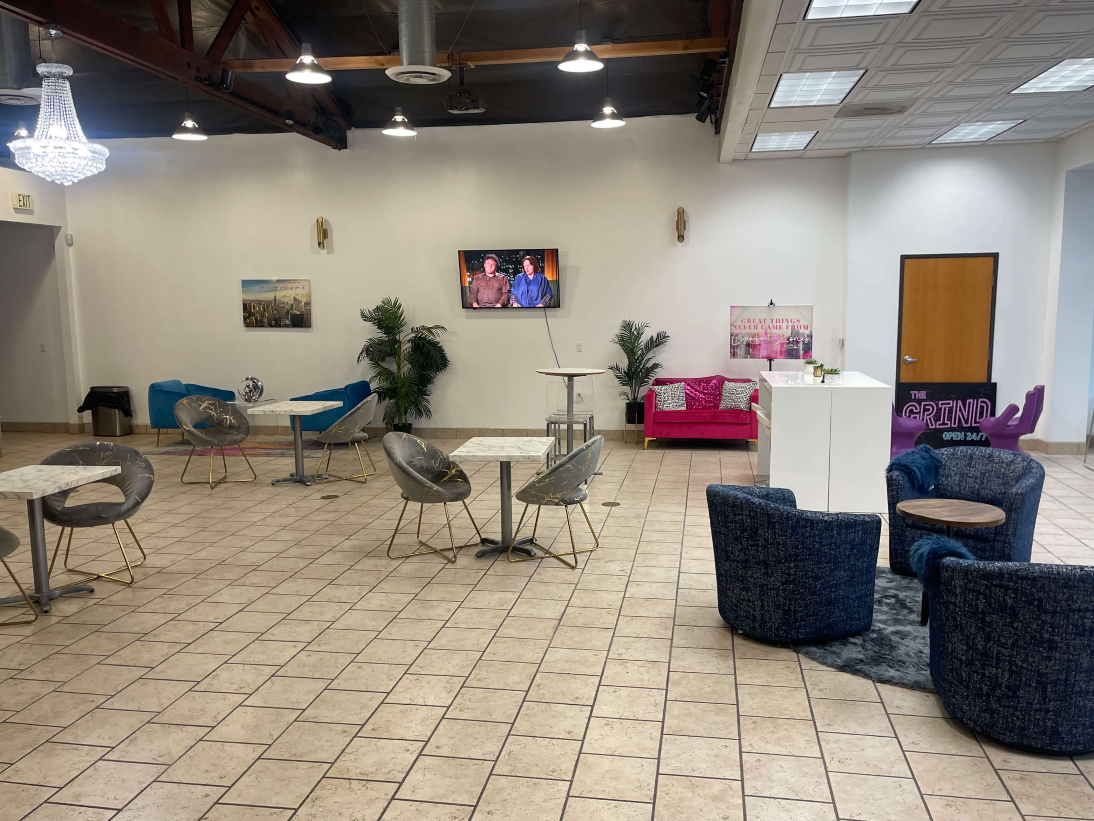 The interior of a spacious event venue features several seating arrangements, including tables and chairs, along with a large television display on one wall.