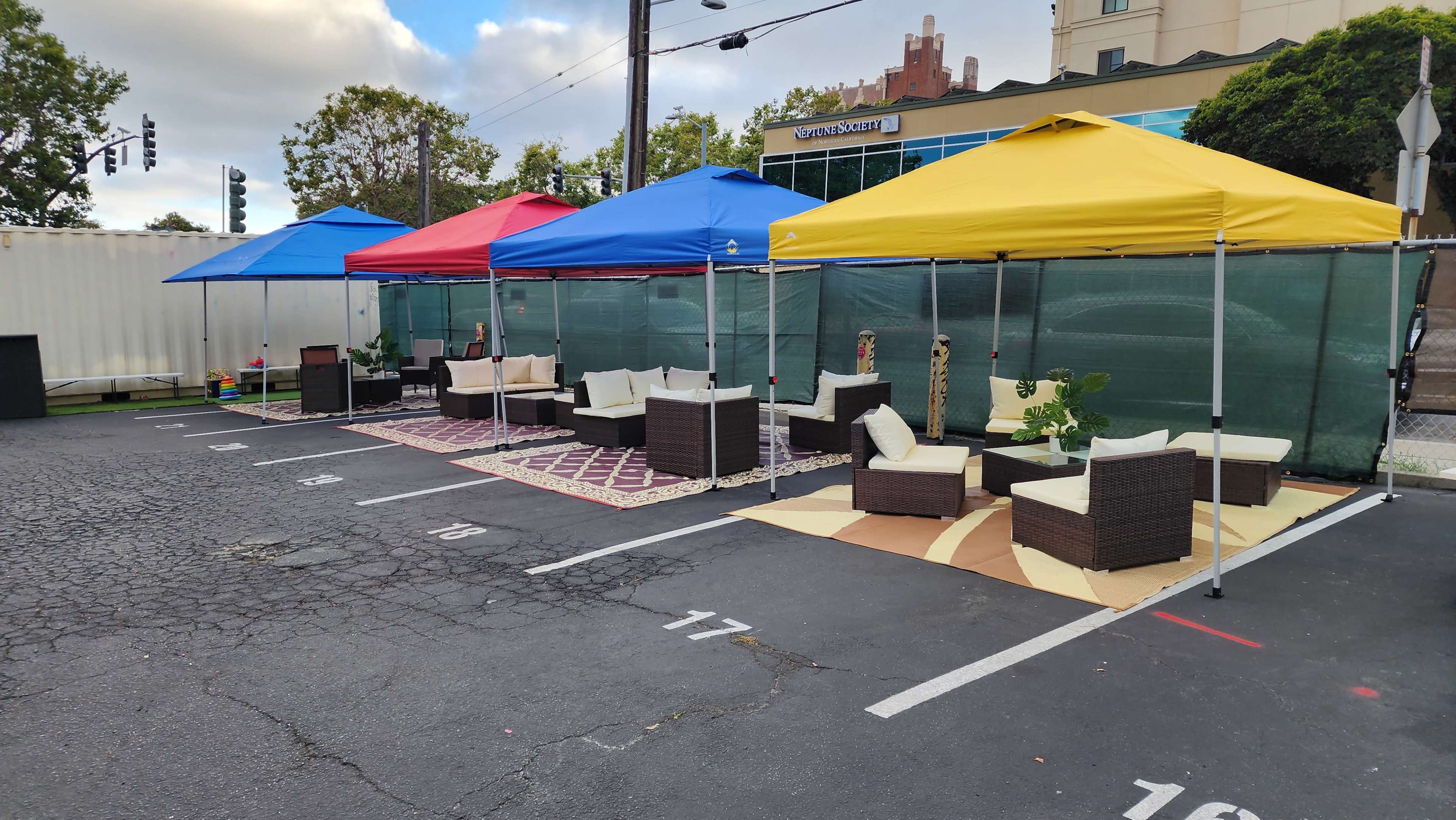 Several outdoor seating arrangements under colored canopies in a parking lot.
