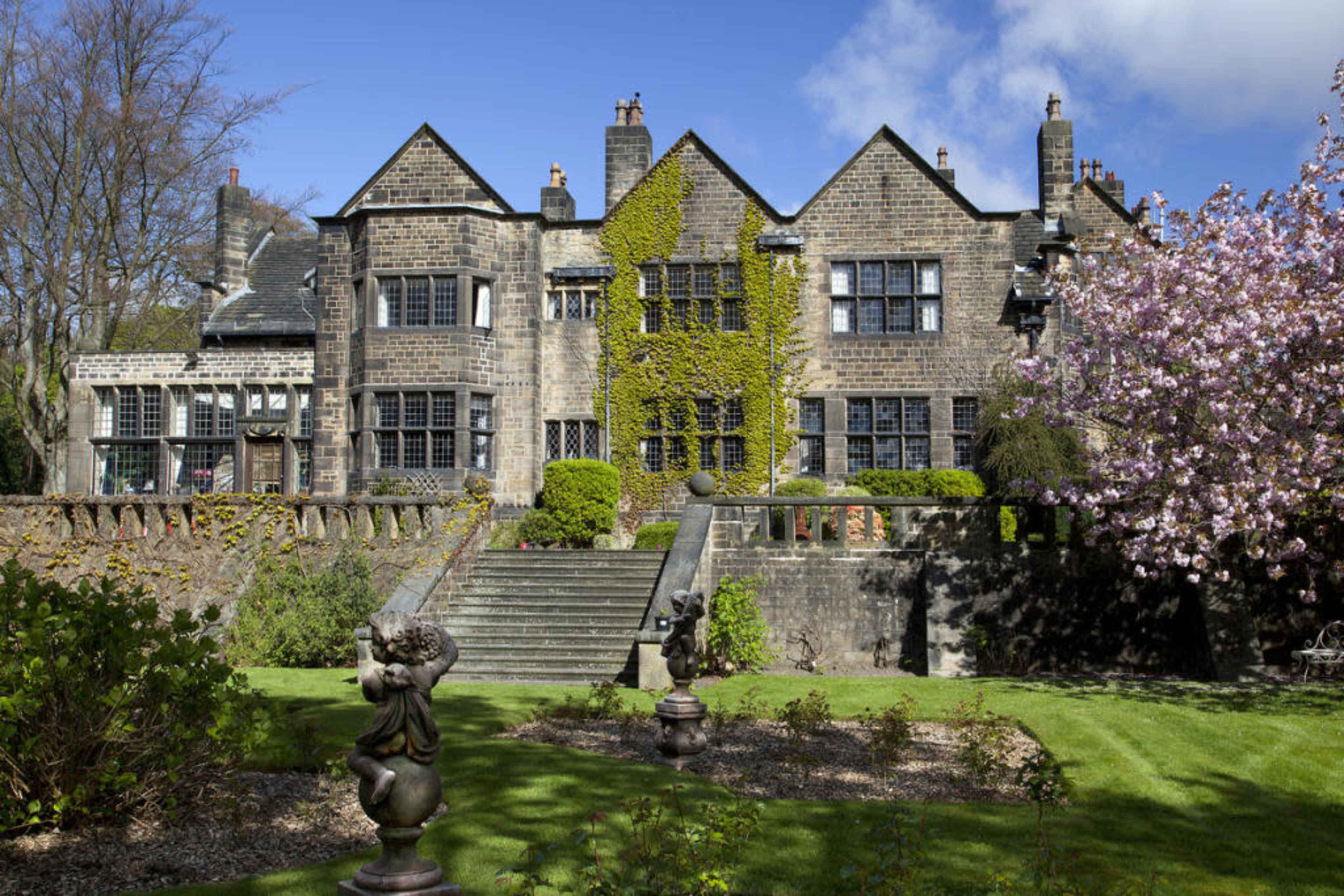 A large stone house with ivy climbing its walls, surrounded by well-maintained gardens and trees.