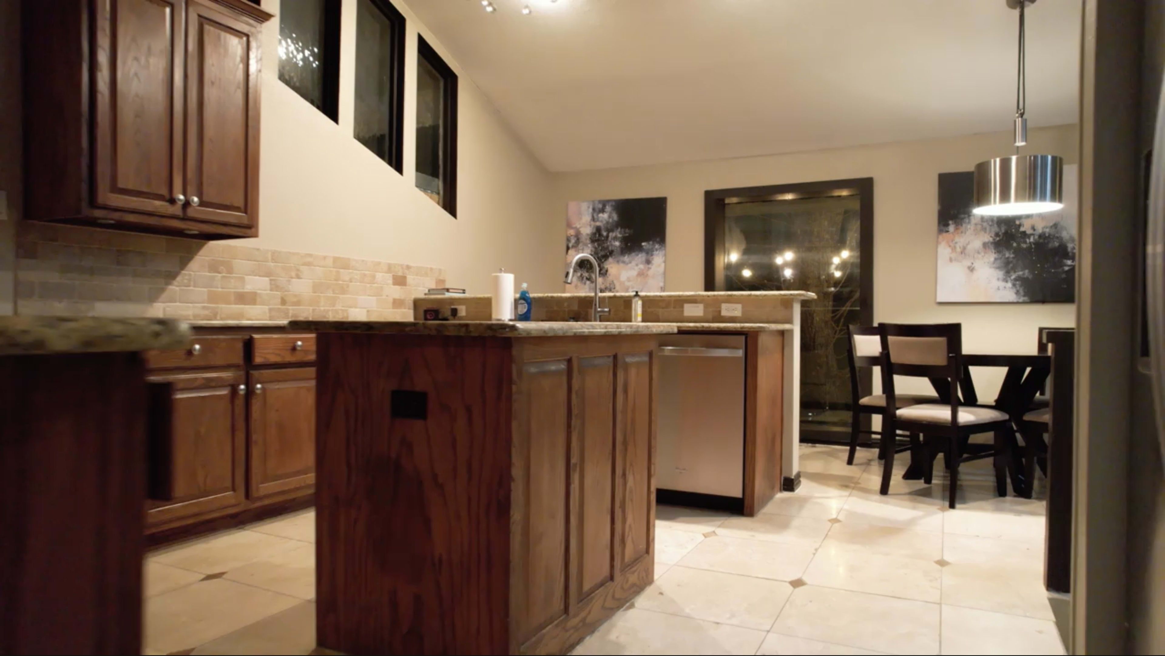 A modern kitchen with wooden cabinets, a central island, and a small dining table with chairs.